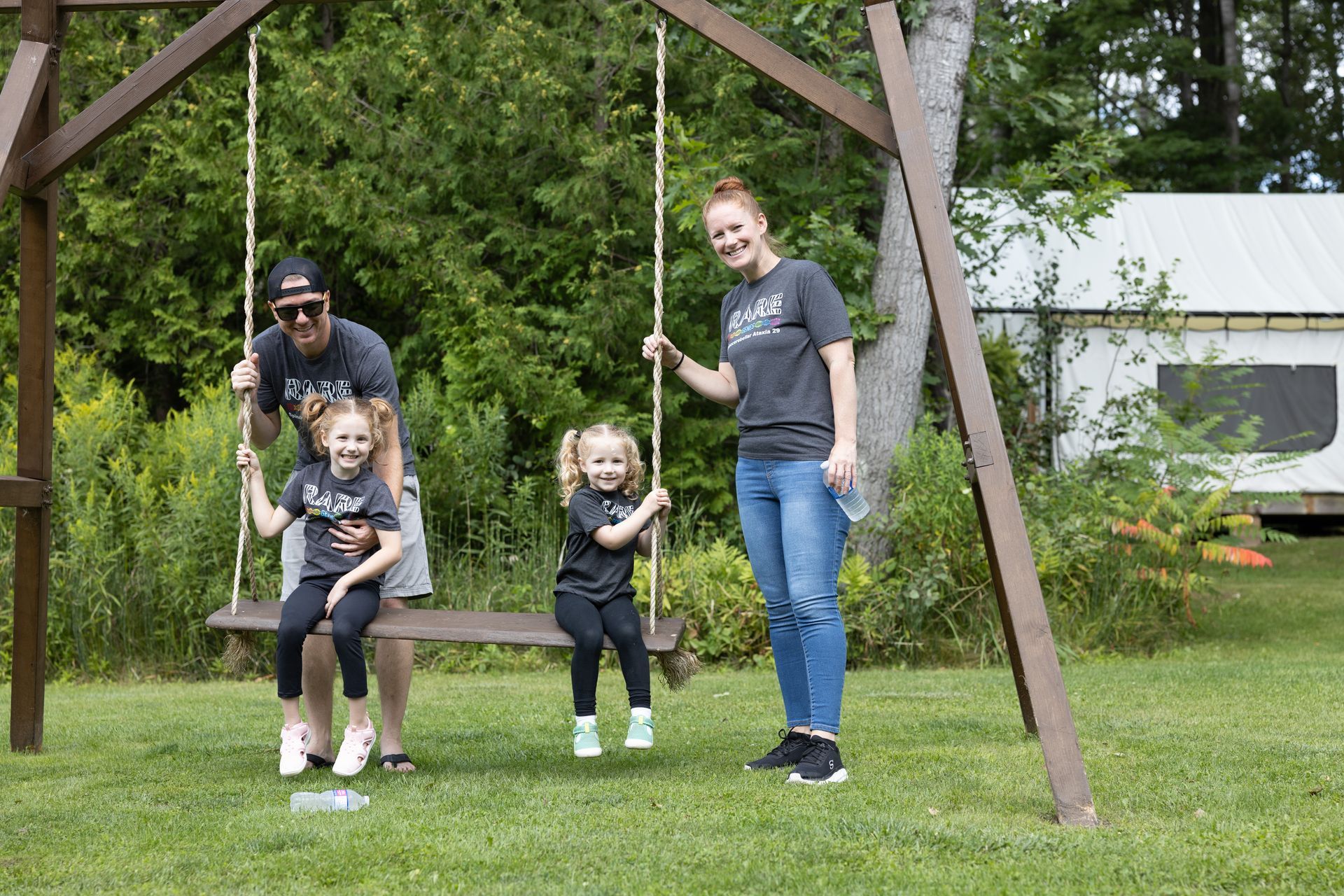 Family of four on a swing set in a grassy yard, smiling.
