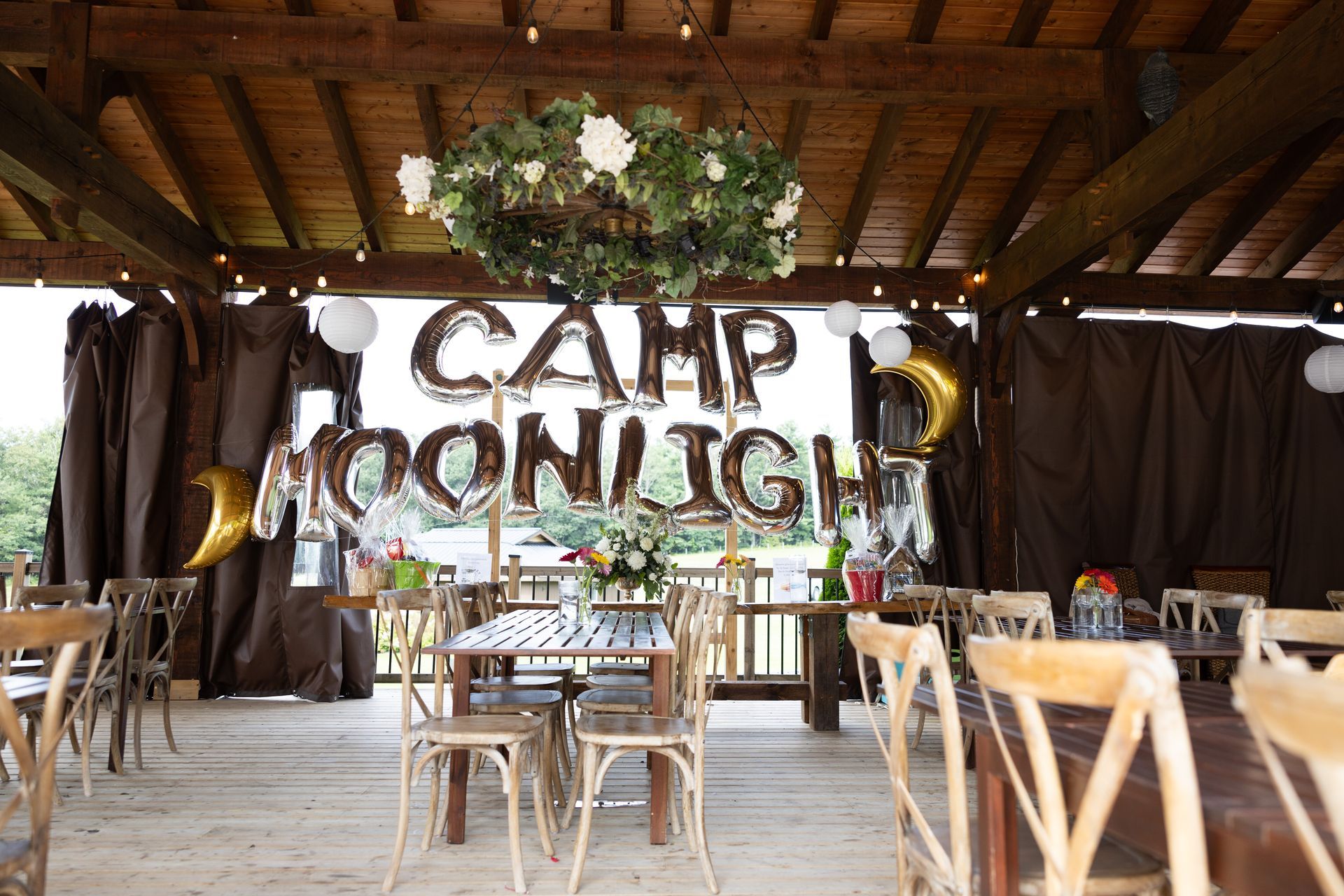 Camp Moonlight party setup with wooden tables, balloons, and floral decorations.