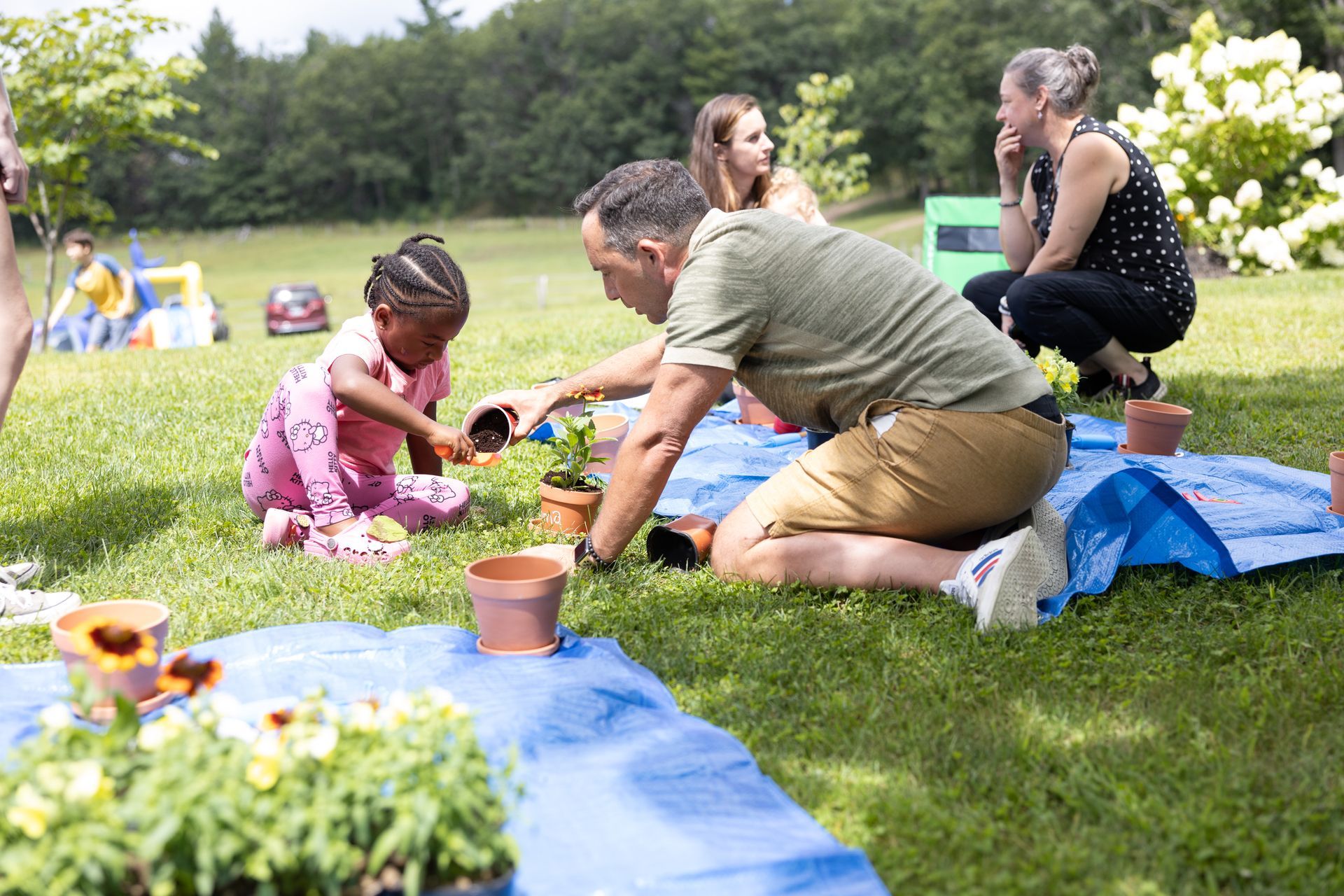 A man and a child plant a flower. They are on a lawn with other adults.