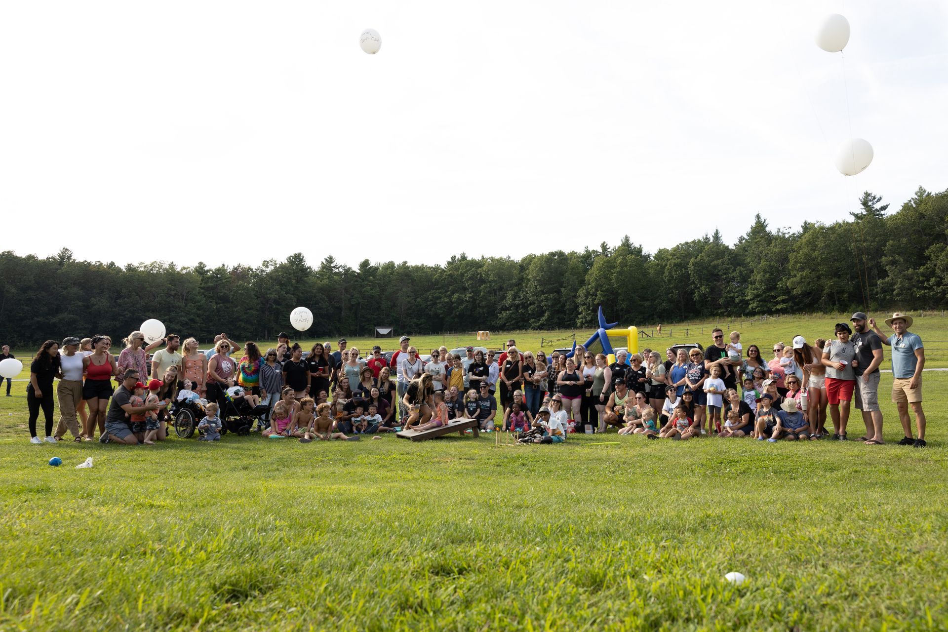 A large group of people gathered in a grassy field, releasing white balloons into the sky.