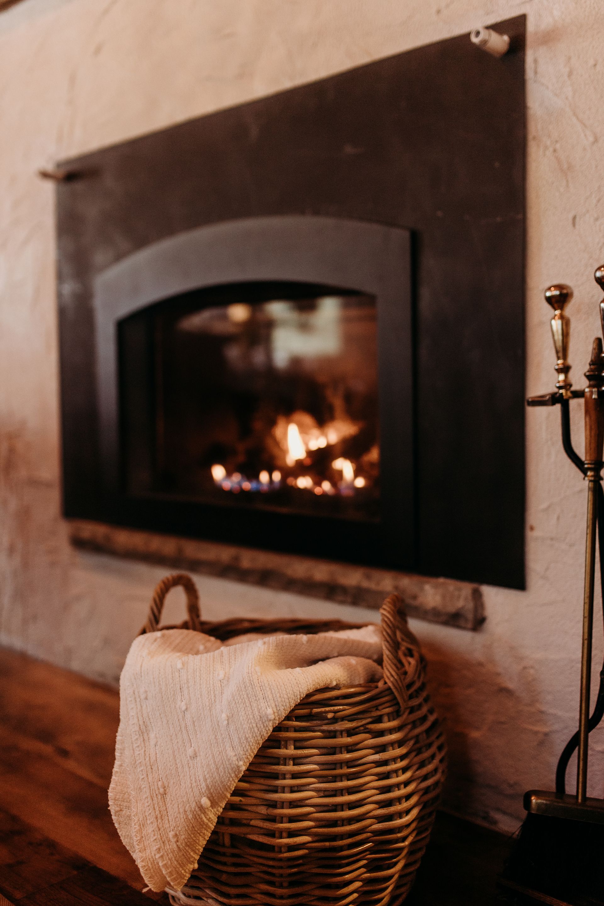 Fireplace with flames, black metal surround, basket with blanket in foreground.
