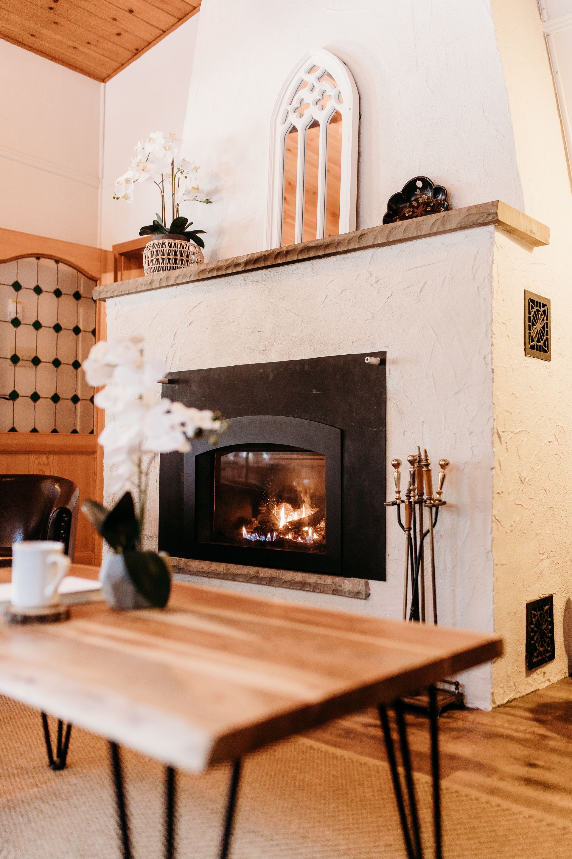 Fireplace with lit fire, wooden mantel and a coffee table with a white mug in a cozy living room.