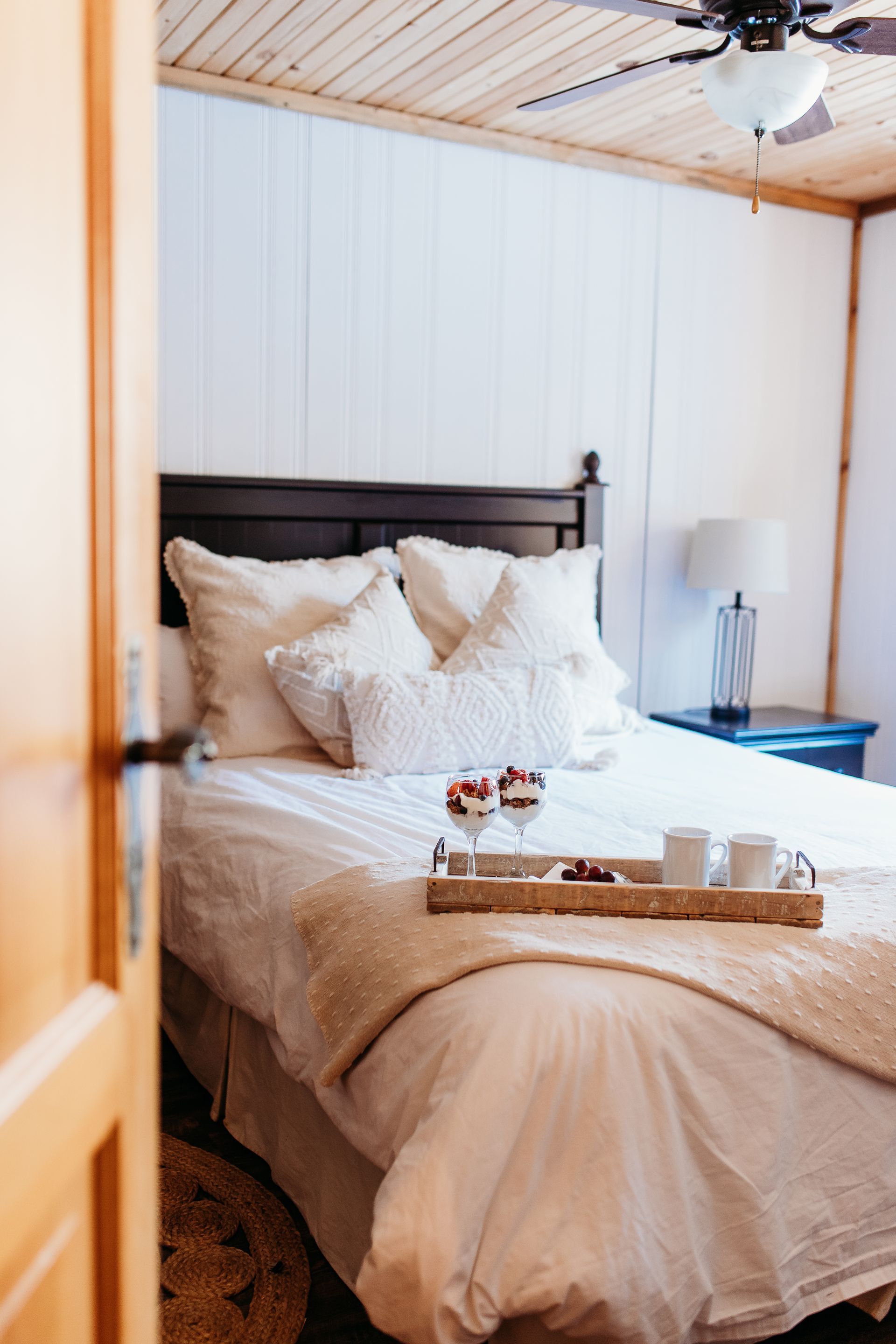 Cozy bedroom with bed, tray of treats, white bedding, dark wood headboard, and wooden door.