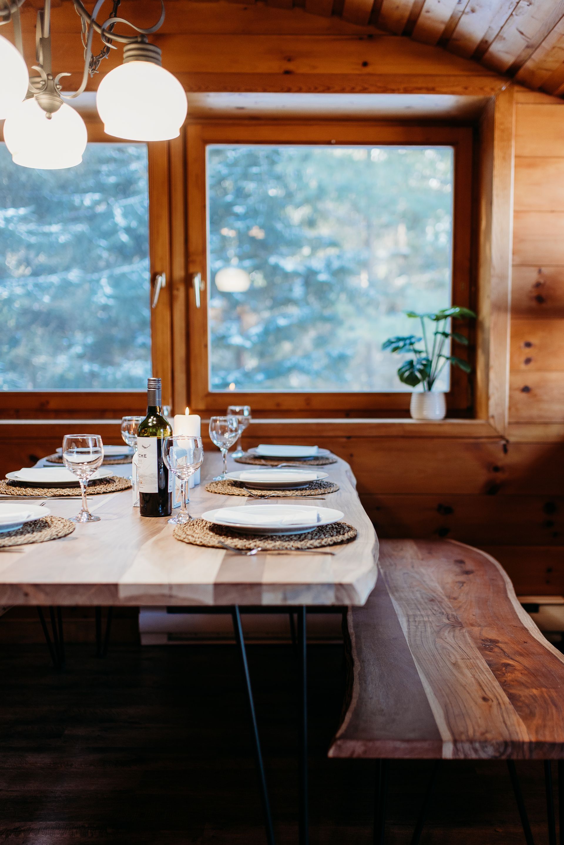 Wooden dining table set for a meal in a cabin, with a window view of trees.