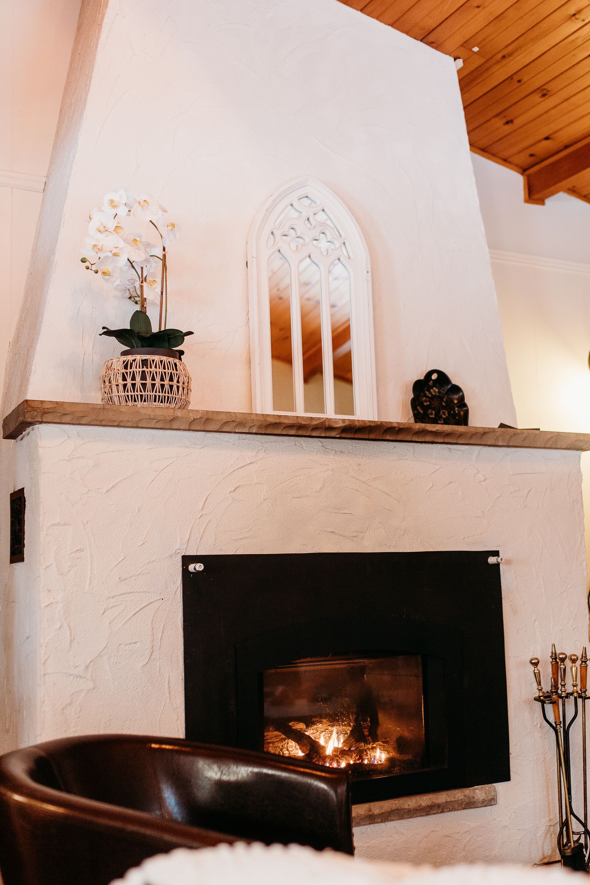 Fireplace with burning fire, decorative mirror, and potted orchid on the mantel.