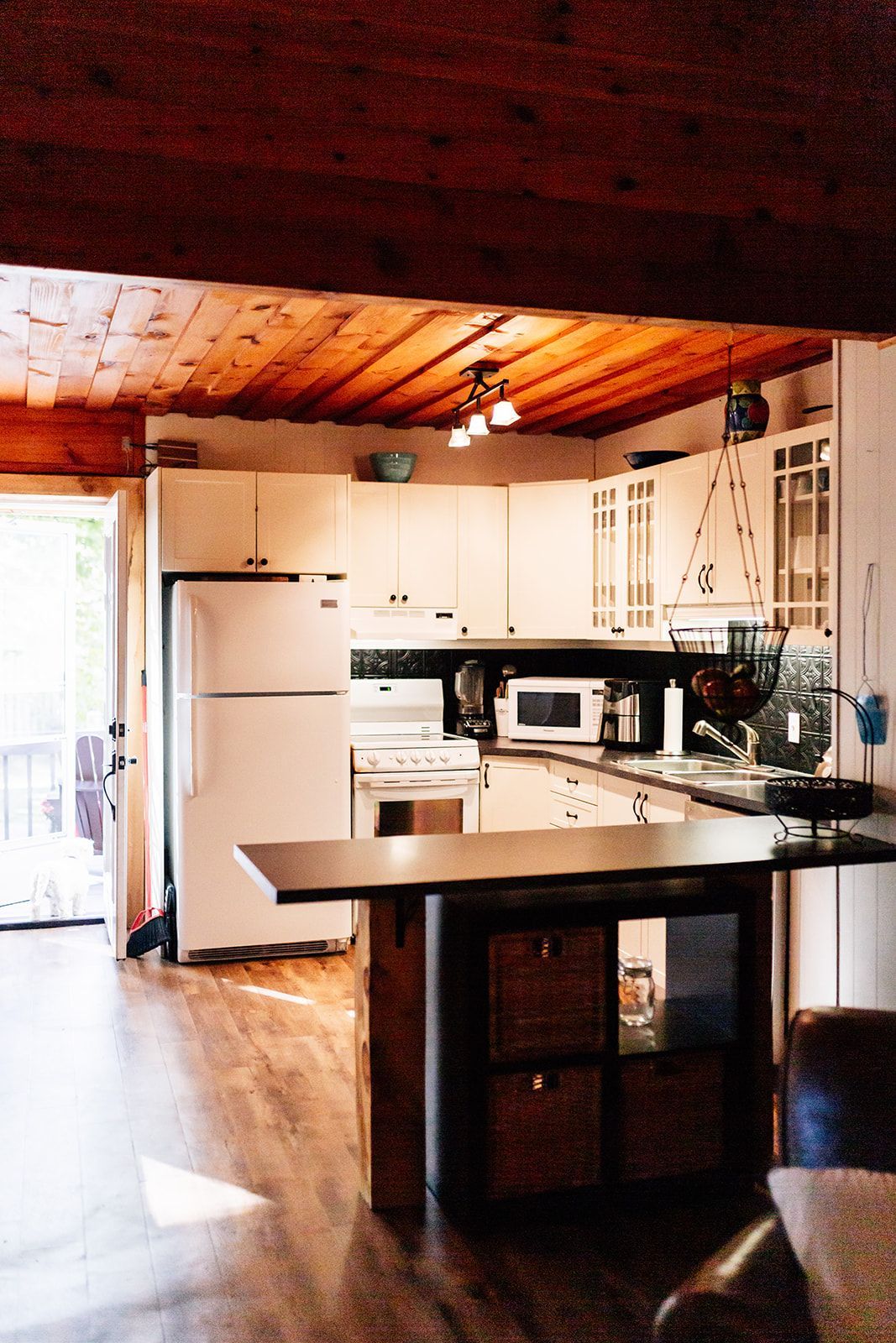 Kitchen with white cabinets, appliances, wooden ceiling, and a dark island.