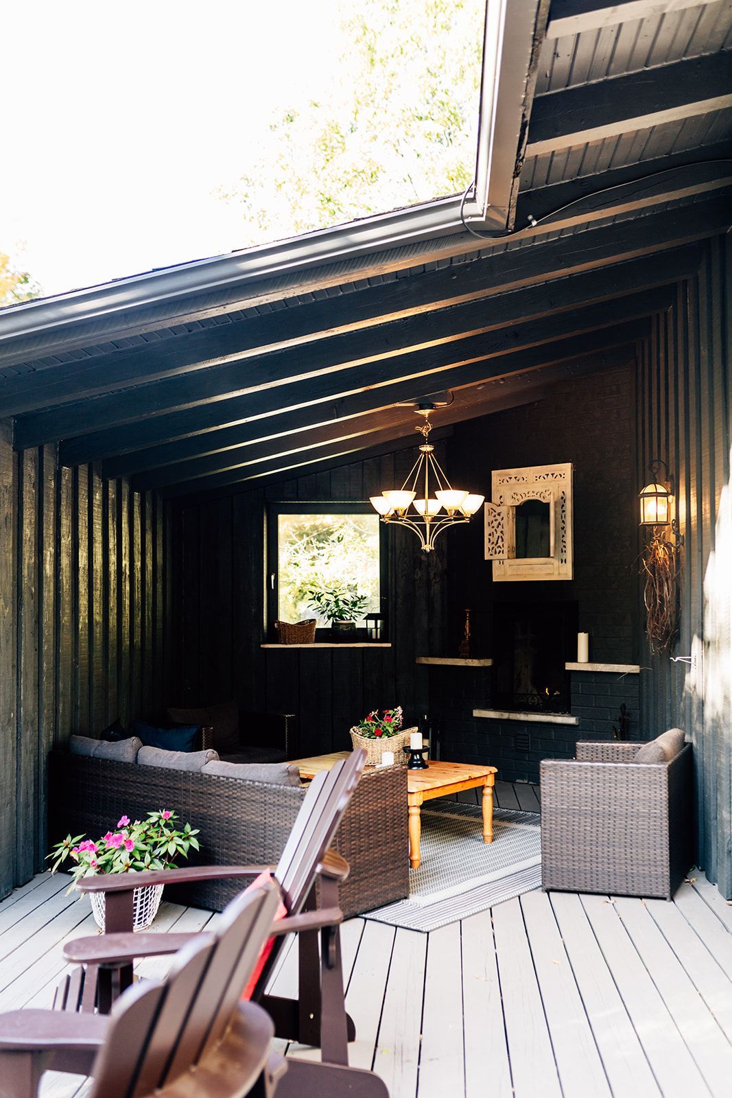 Outdoor living space with dark wood paneling, wicker furniture, and a chandelier.