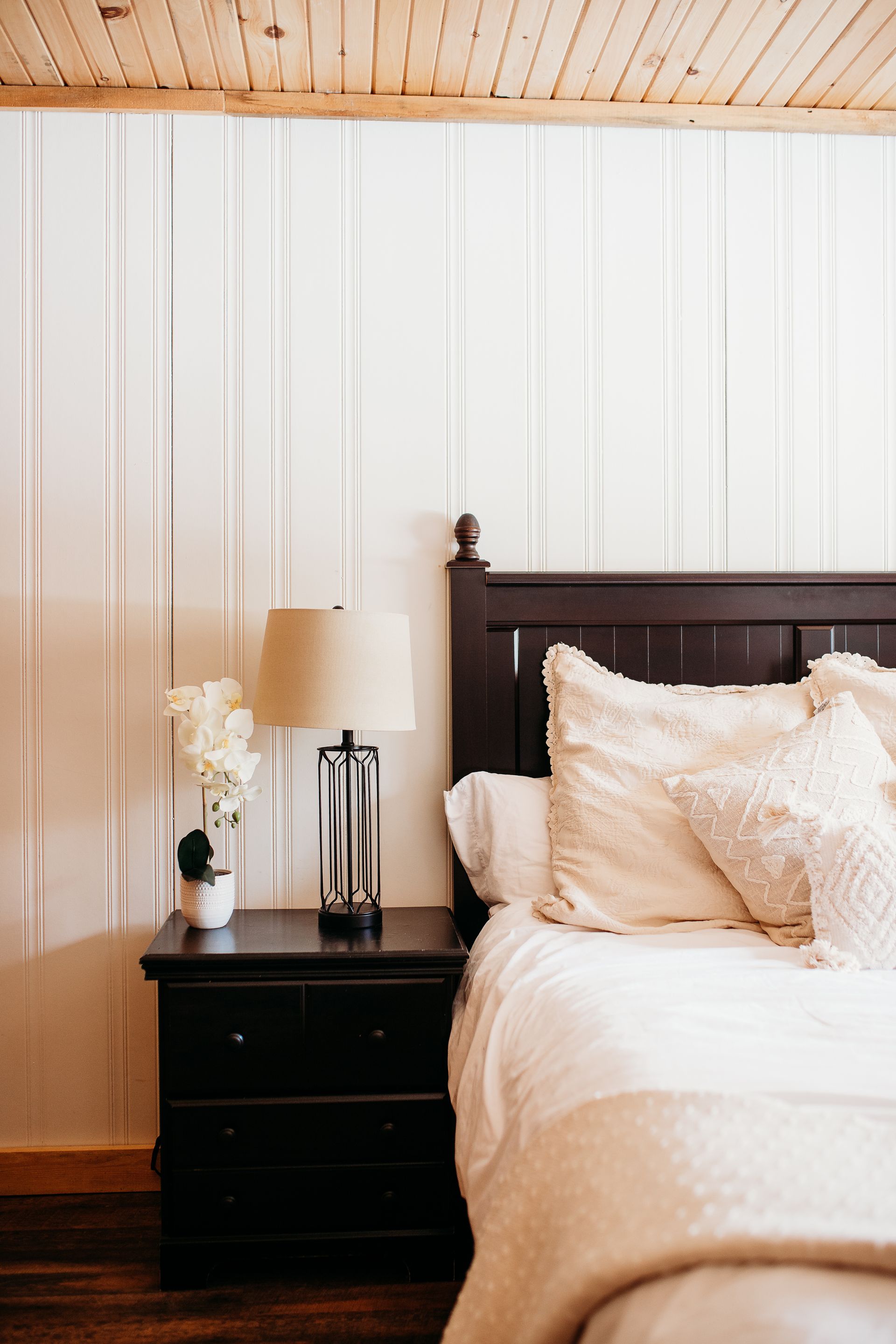 Bedroom with a dark wooden nightstand, bed, and white beadboard walls.