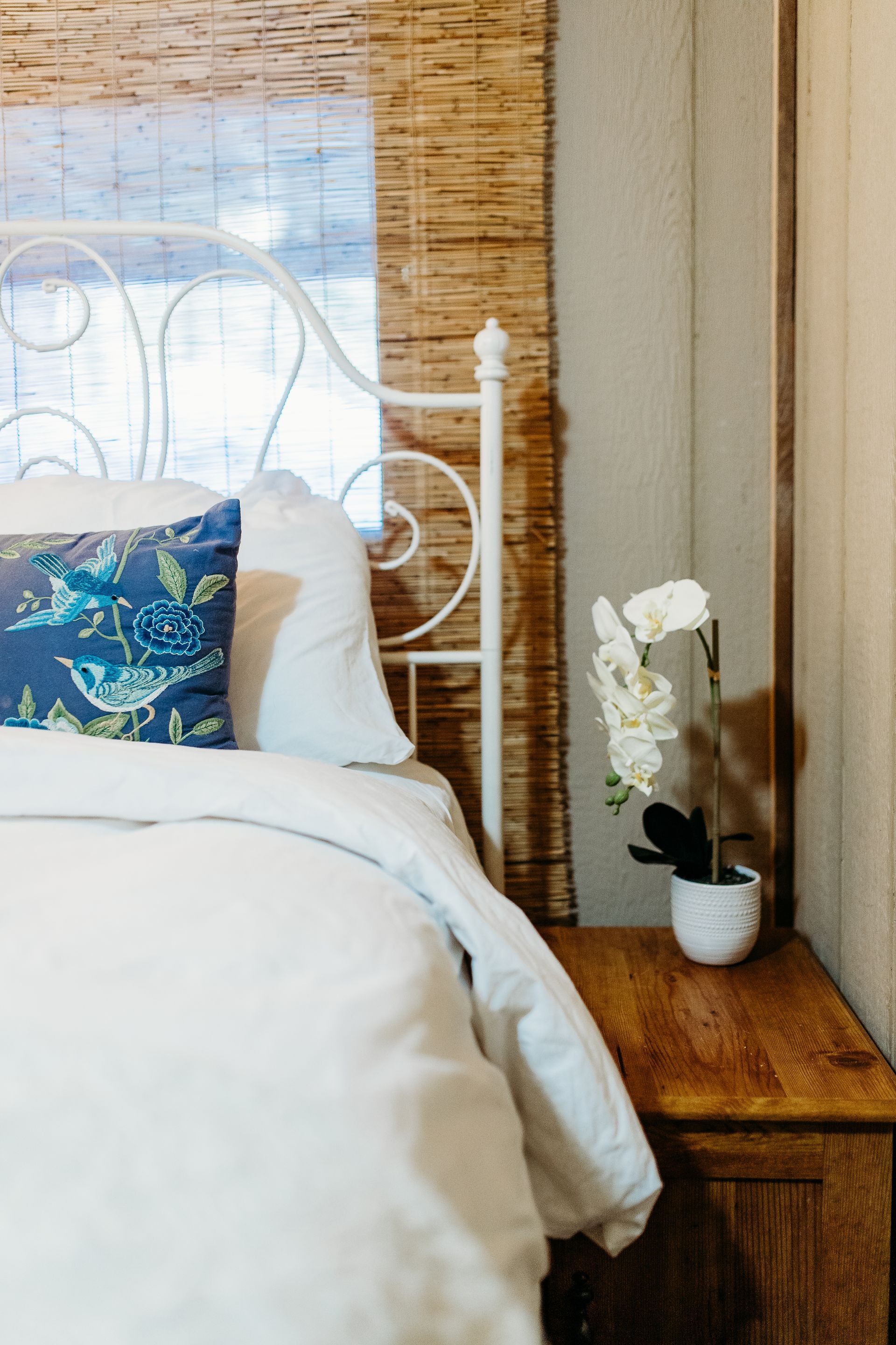 White bed with ornate headboard, blue pillow, and nightstand with orchid plant.