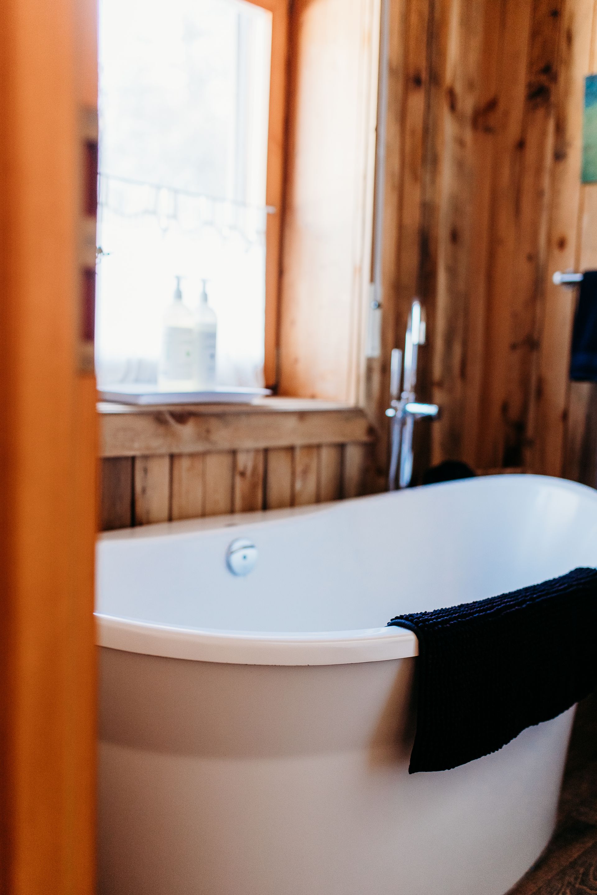 White bathtub in a wooden-paneled bathroom, with a window and faucet visible.