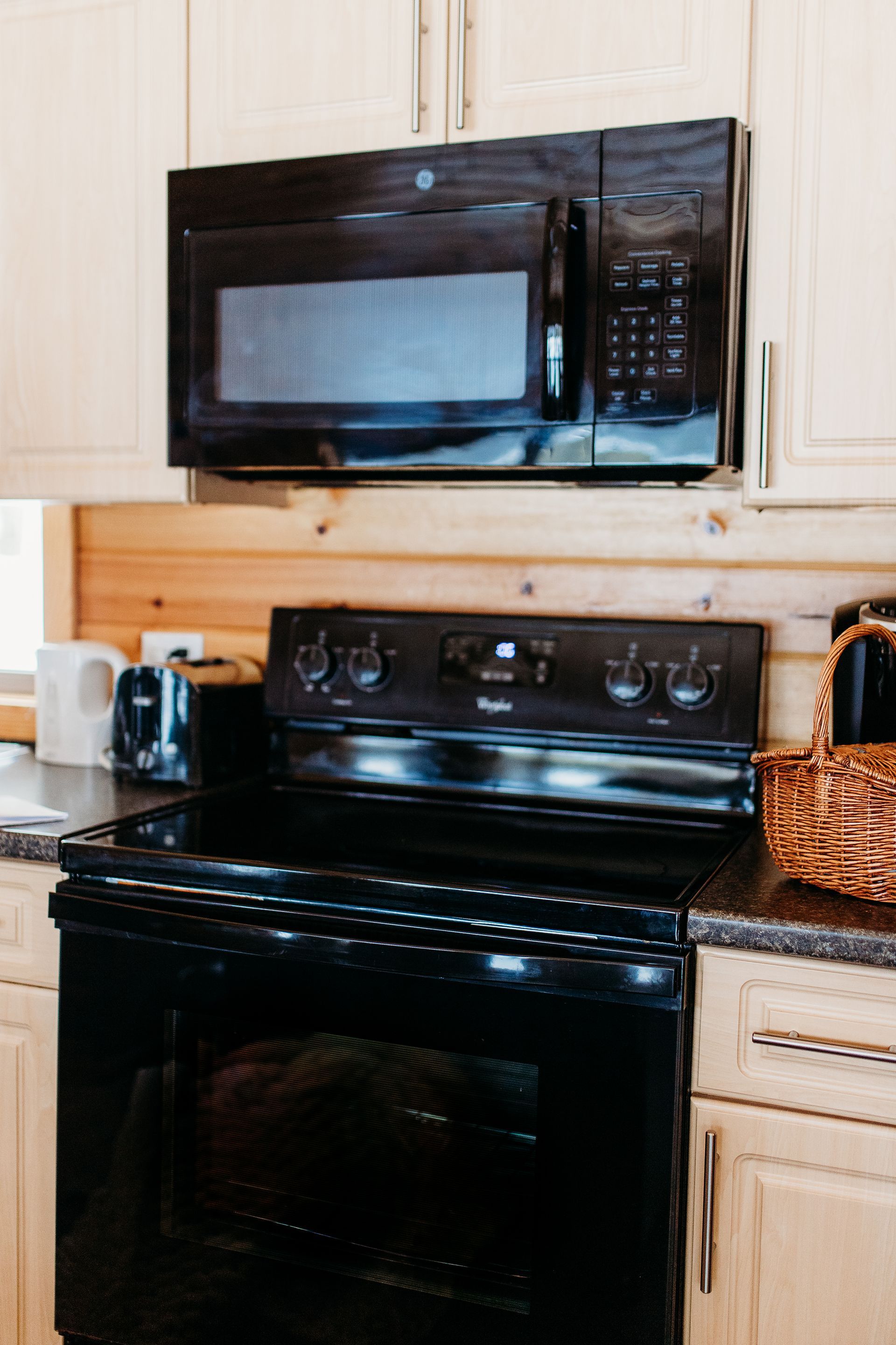 Black microwave above a black electric stove in a kitchen with cream cabinets.