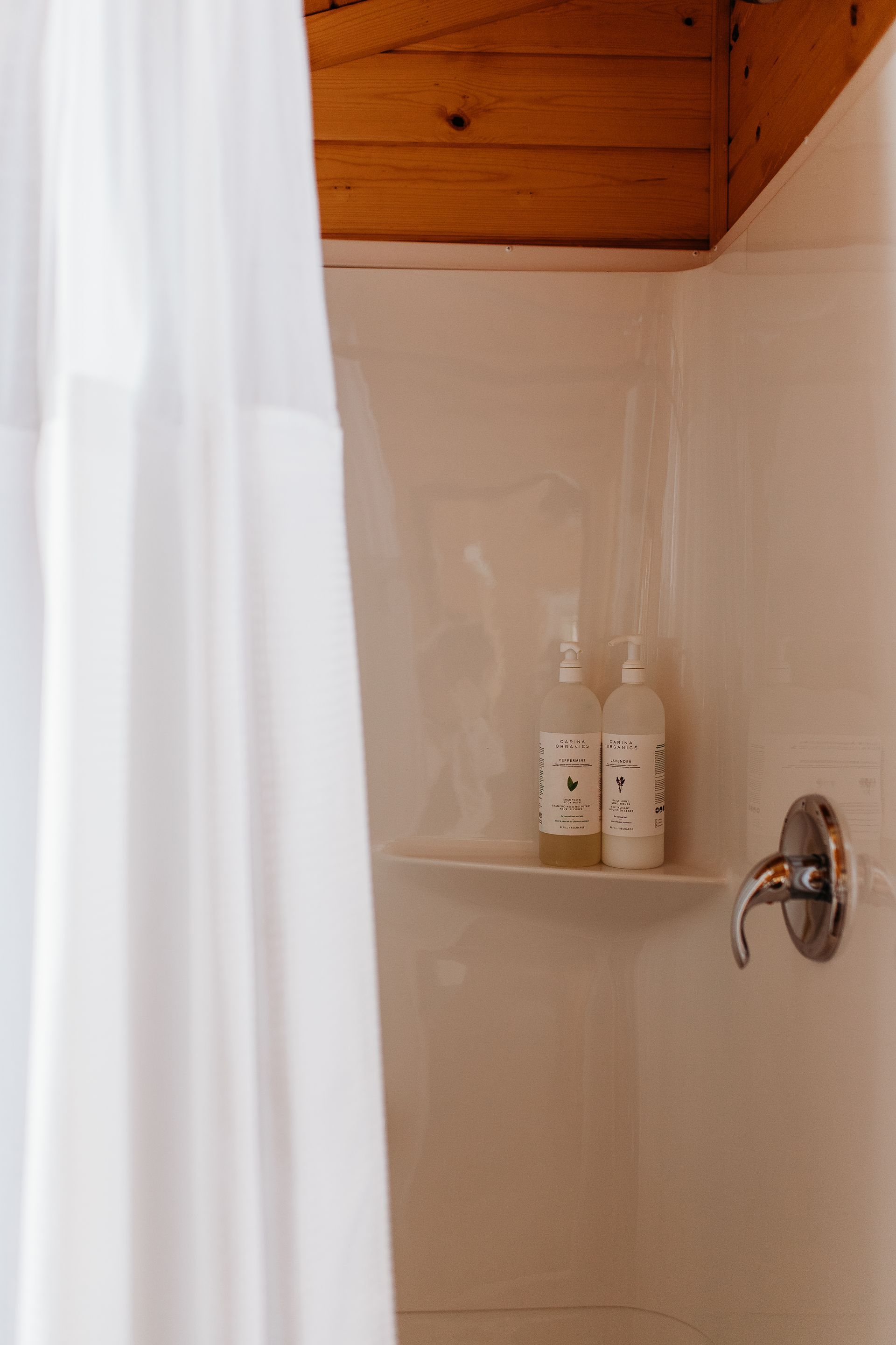 White shower with white bottles on a shelf, partially obscured by a white shower curtain.