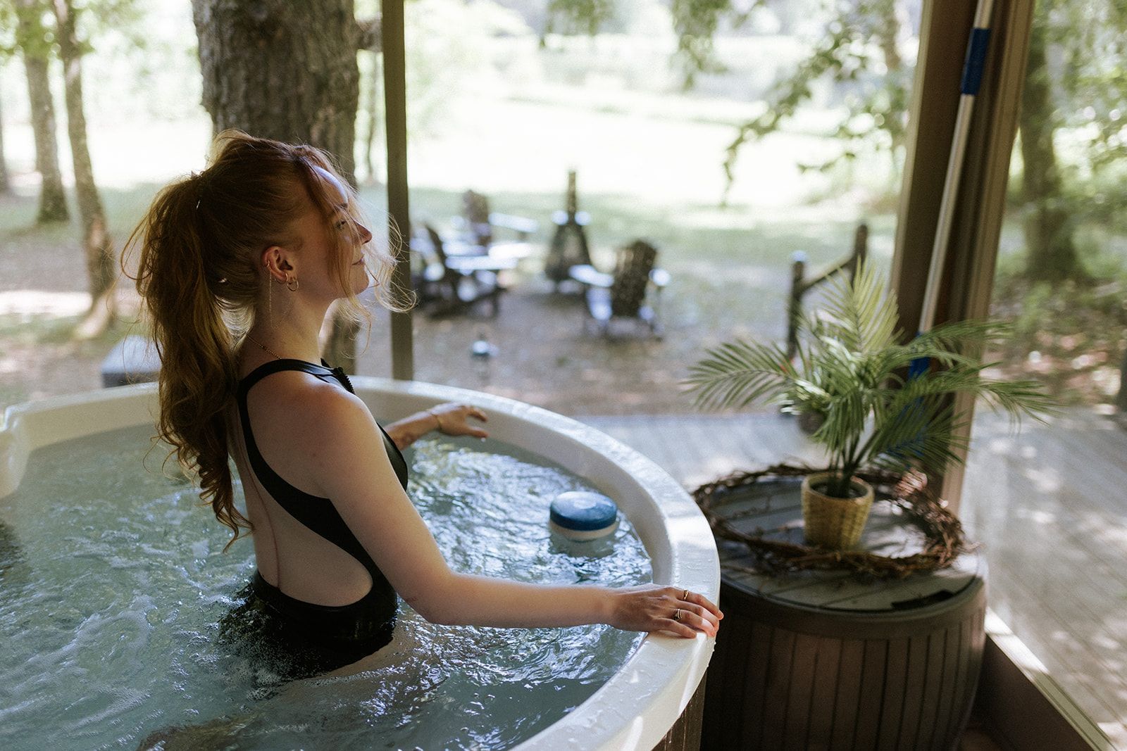 Woman in a black swimsuit relaxing in a hot tub outdoors, looking away with a peaceful expression.