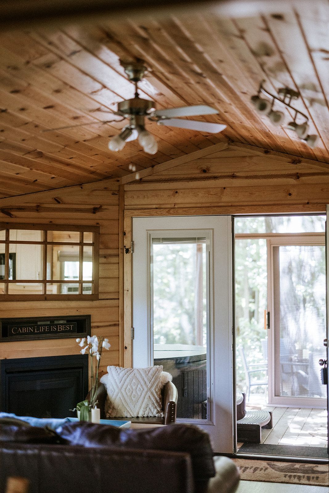 Cozy cabin interior with wooden walls and ceiling, a fireplace, and a doorway leading outside.