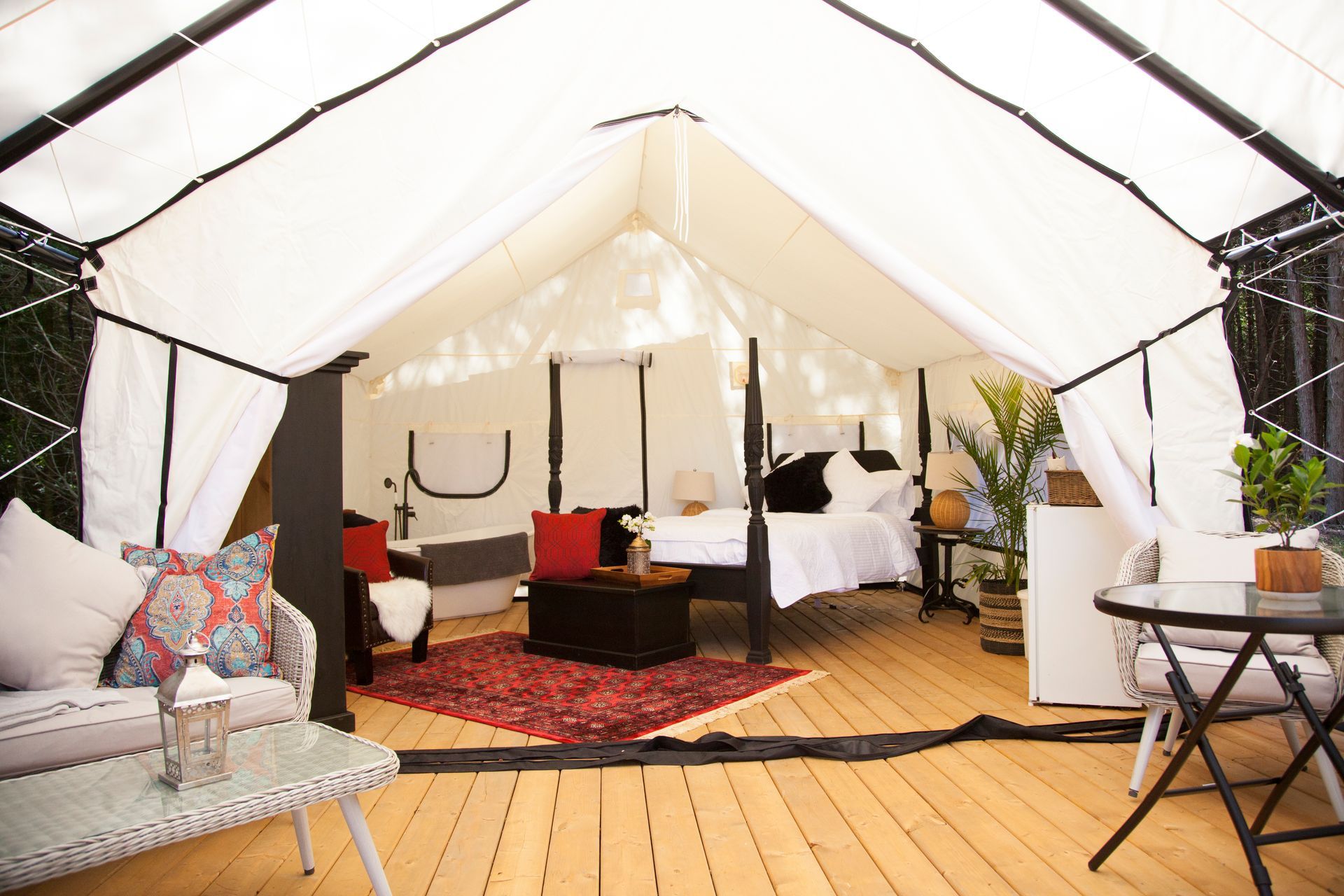 Spacious glamping tent interior with bed, couch, and table on a wooden floor.