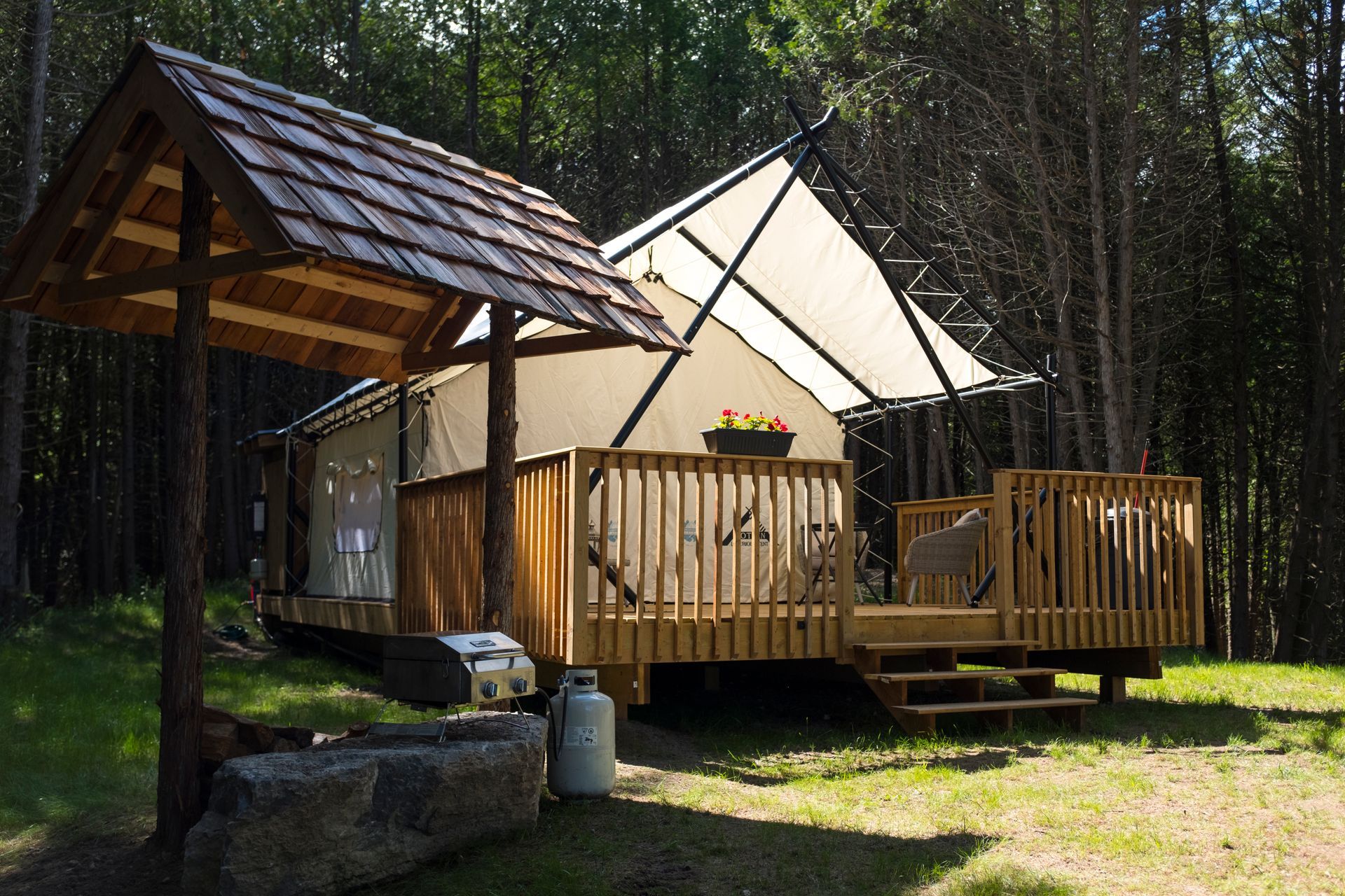 Glamping tent with wooden deck, awning, and decorative well in a forest setting.