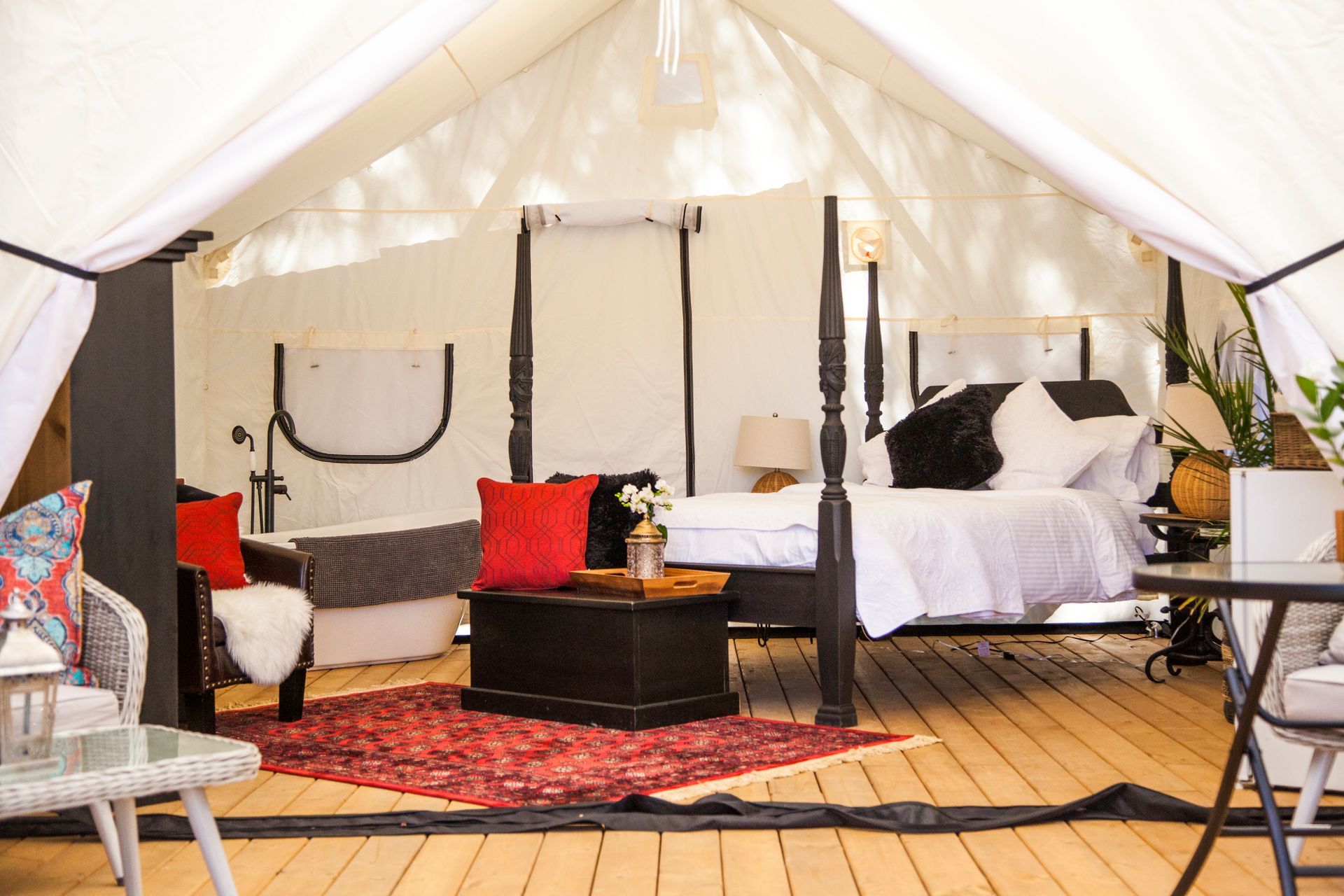 Inside of a luxurious tent; bed, furniture, red rug, cushions, and wooden floor.