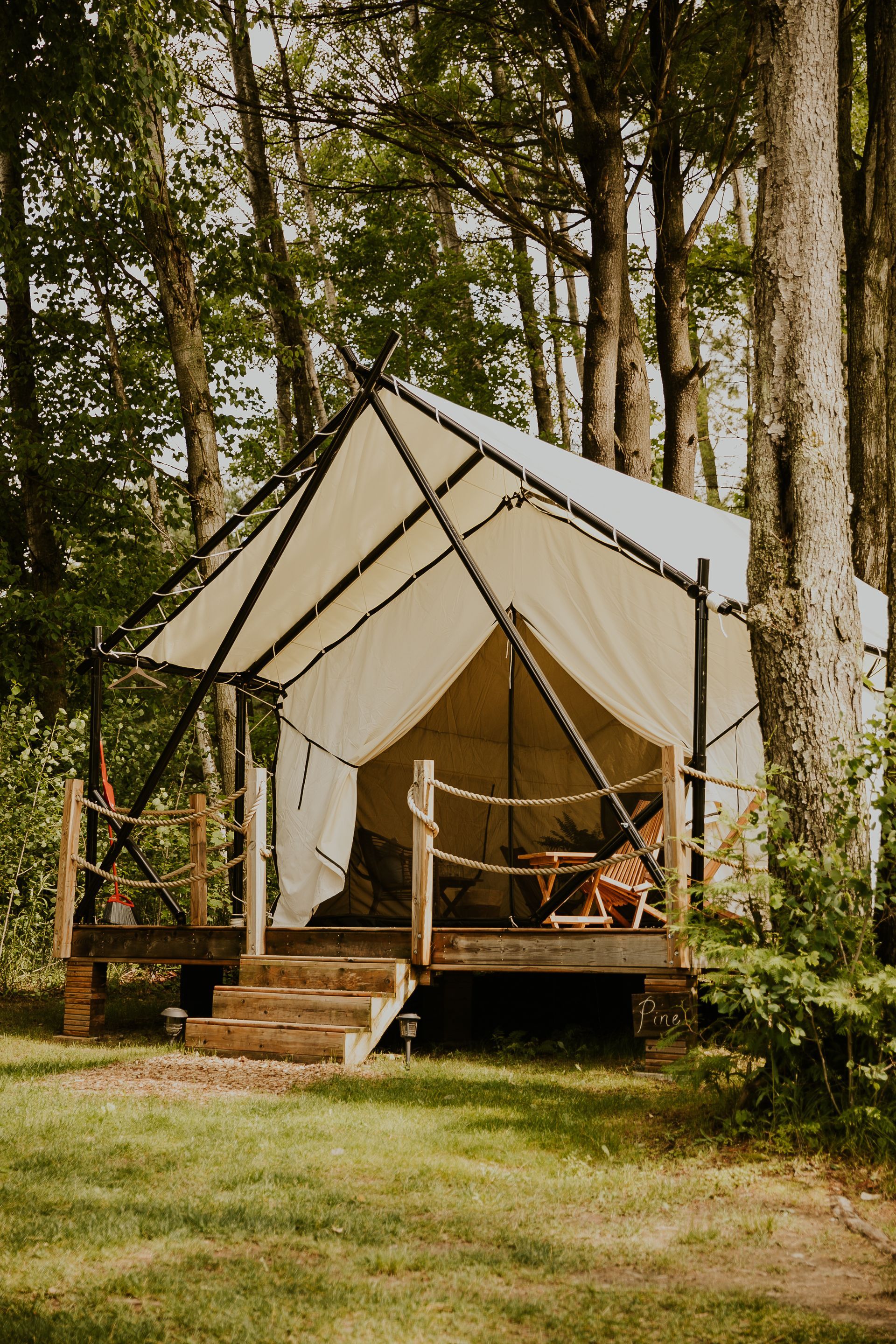 Canvas tent on a wooden deck in a wooded area, with stairs leading up and a rope handrail.