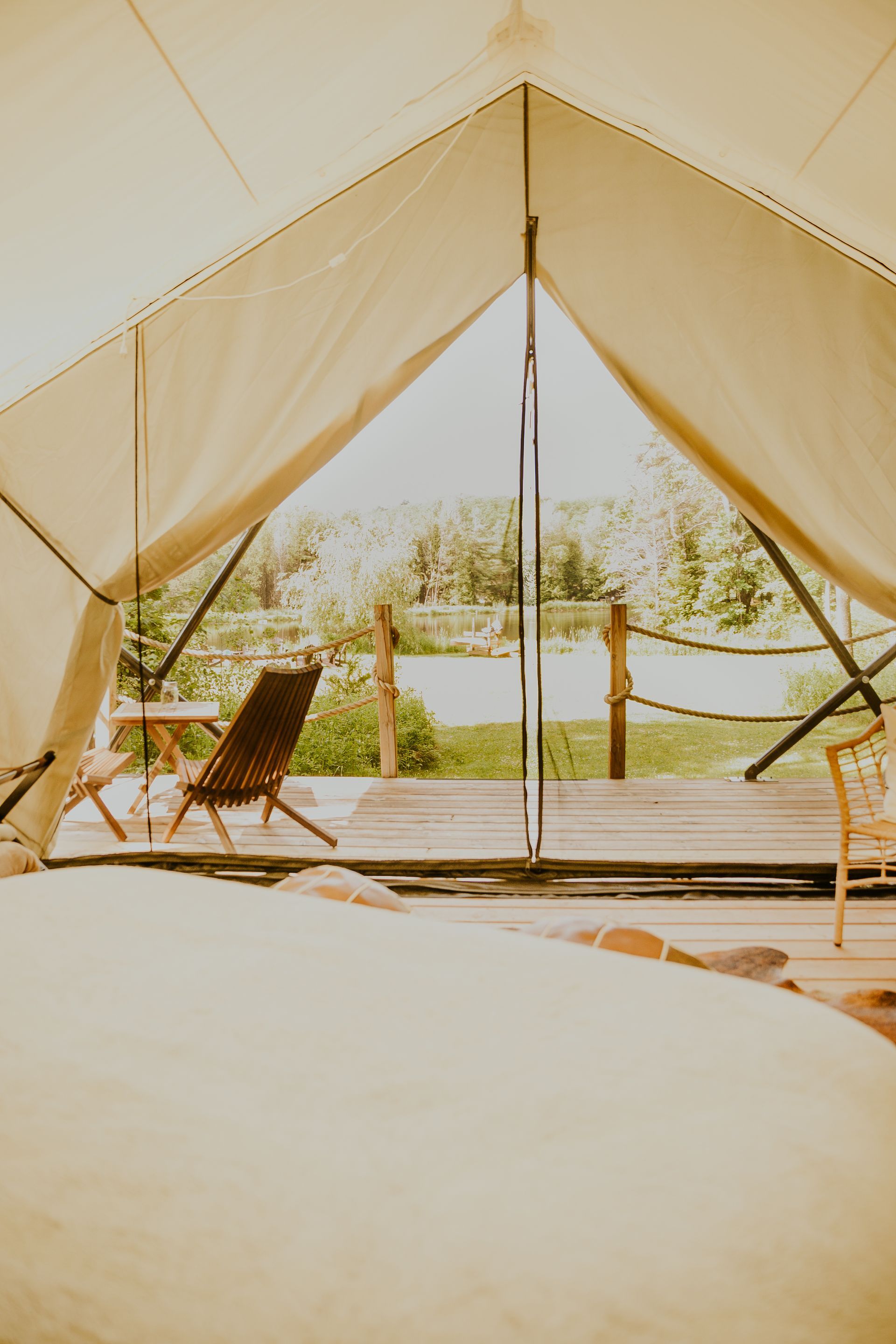 View from inside a tent, looking out onto a wooden deck with a chair and a scenic view of a river and trees.
