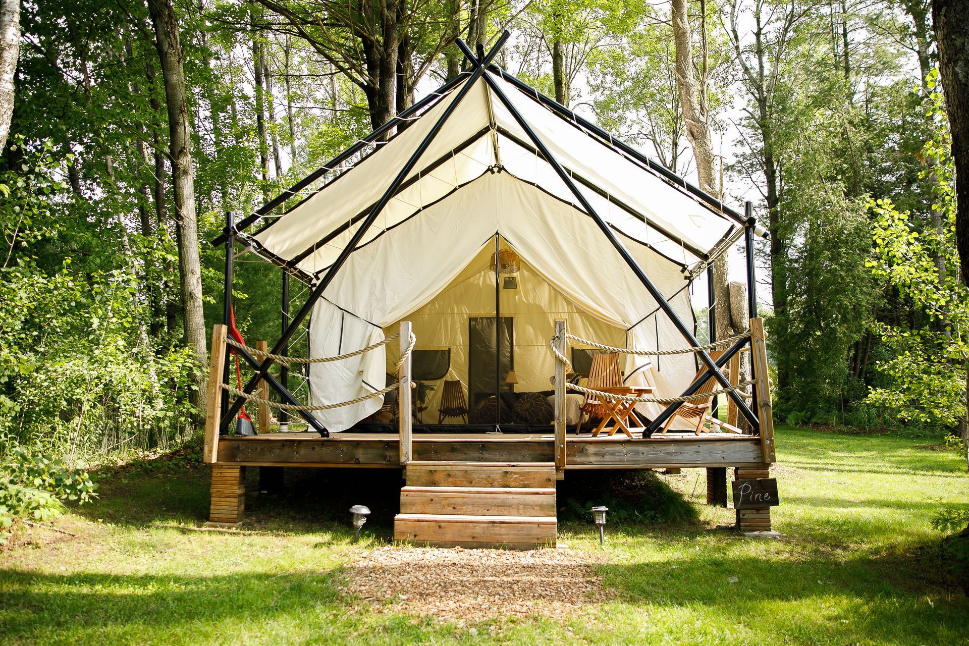 Canvas tent on a wooden deck in a wooded area; front porch with stairs.