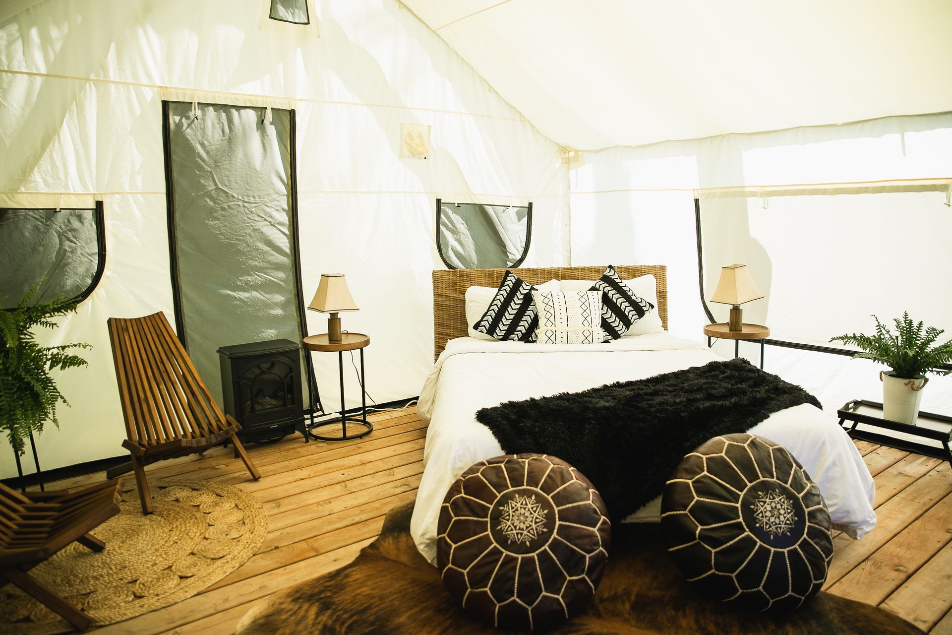 Glamping tent interior with bed, seating, plants, and wooden floor.
