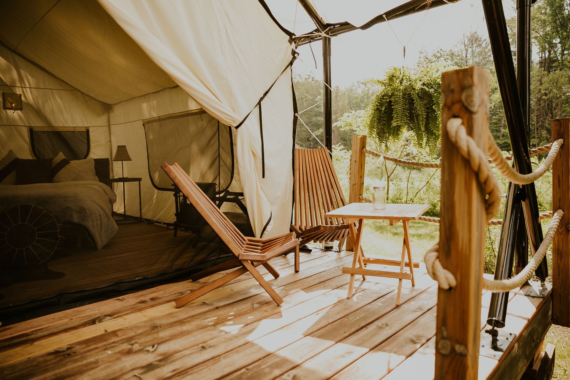 Glamping tent with wooden deck and furniture overlooking a natural setting.