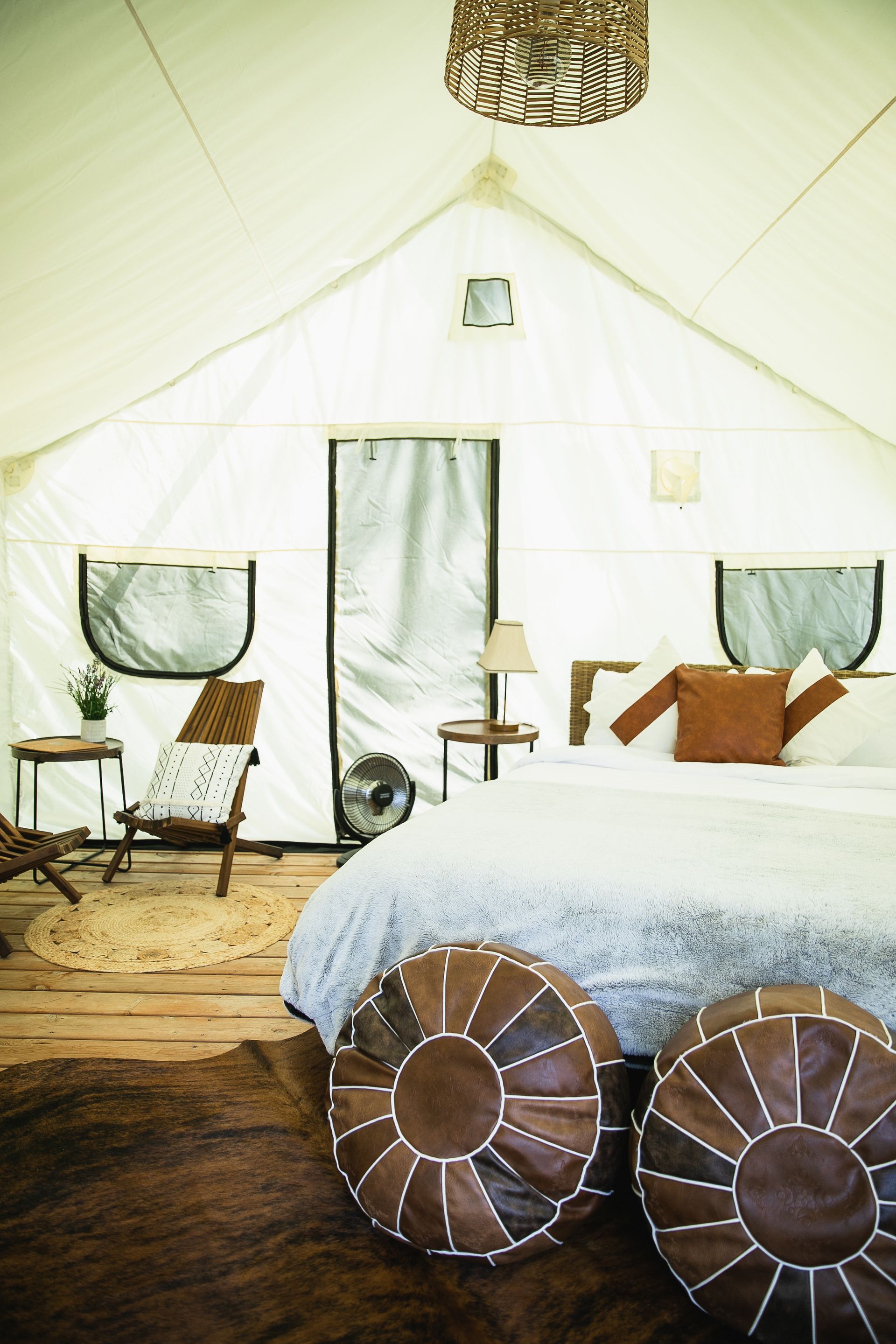 Spacious glamping tent interior with bed, leather poufs, woven rug, and chair.