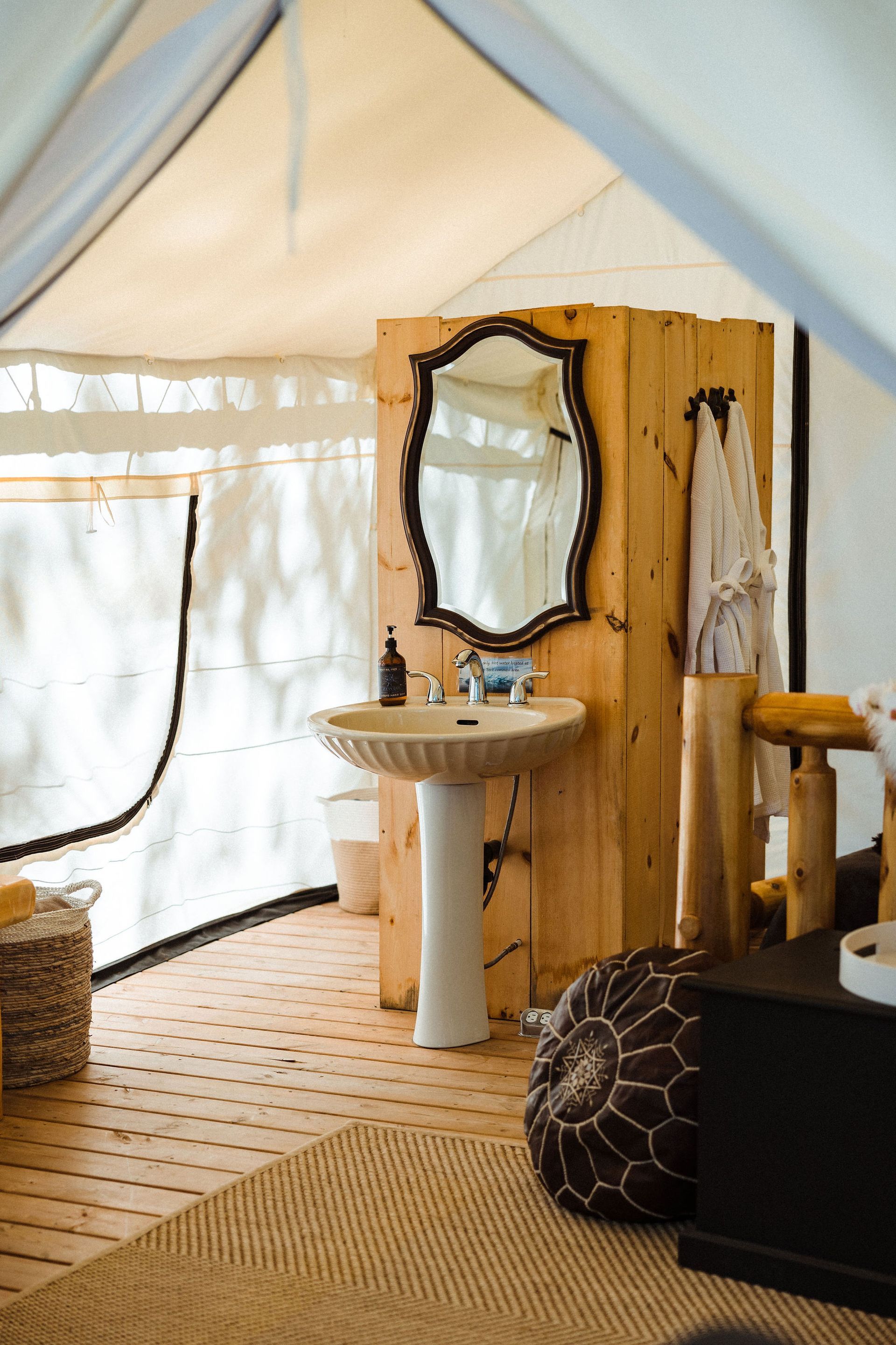 Bathroom inside a tent, featuring a pedestal sink, wood paneling, ornate mirror, and natural accents.
