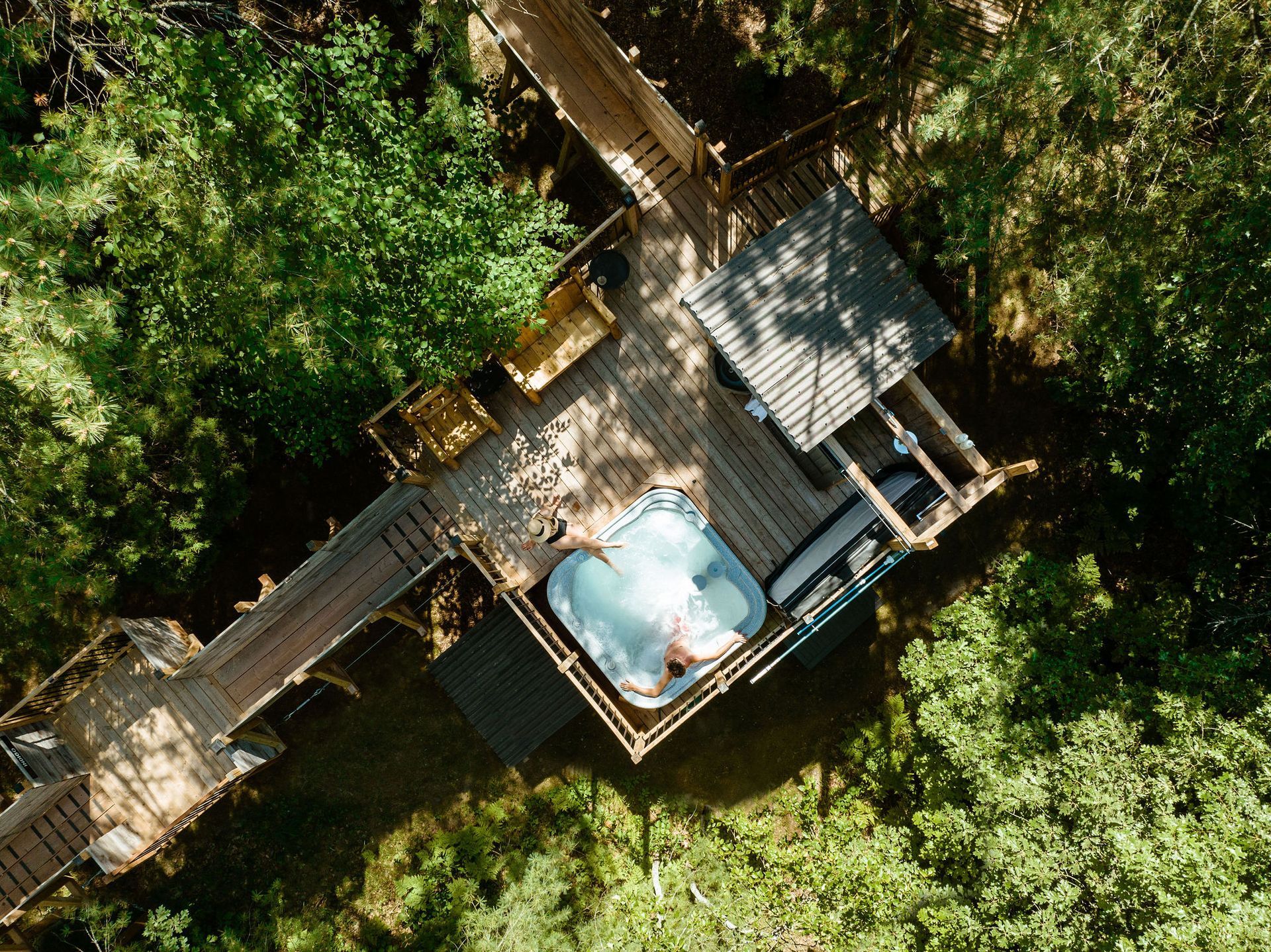 Aerial view of a treehouse with a hot tub on a wooden deck in a lush forest.