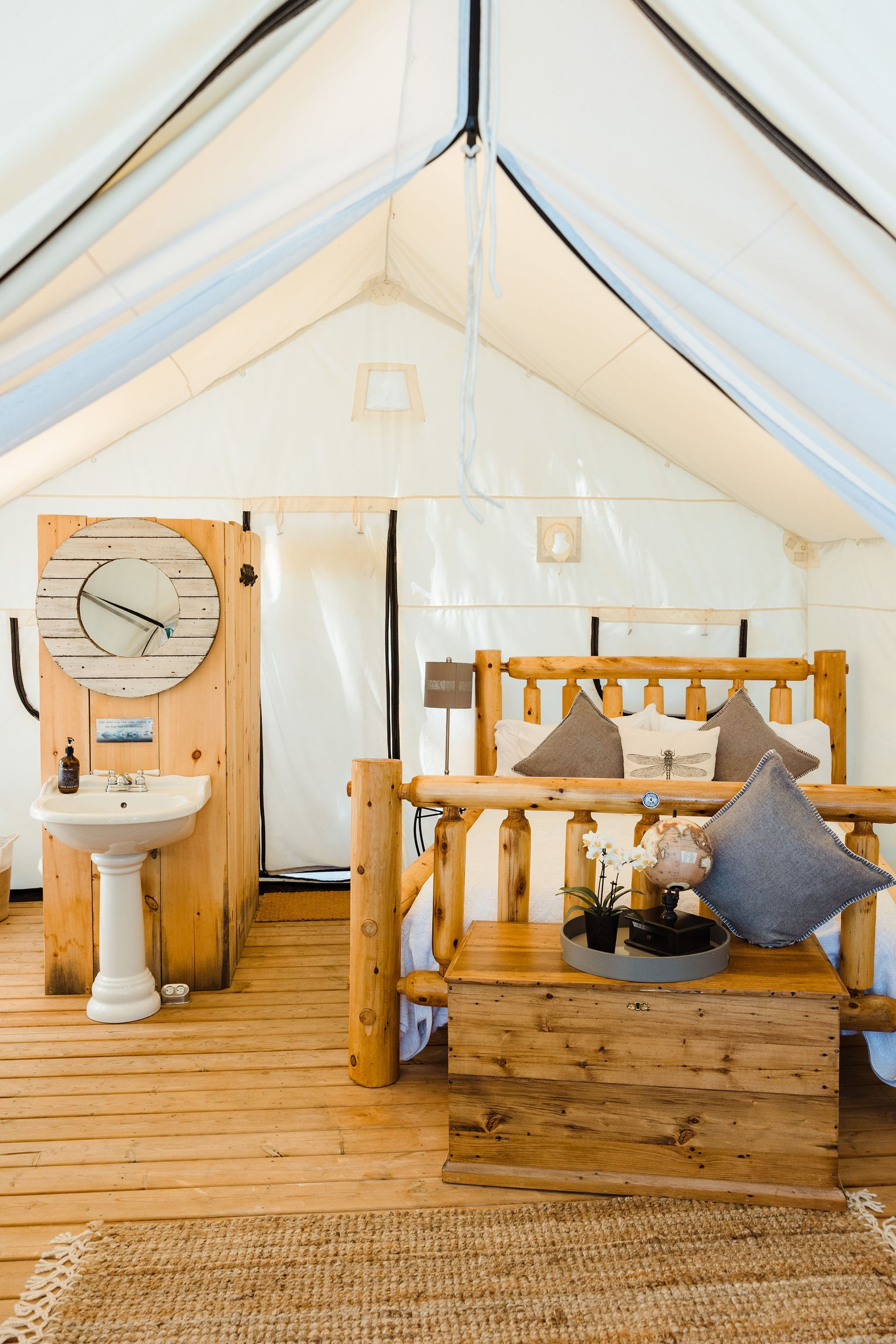 Interior of a glamping tent with wooden bed, washbasin, and rug.
