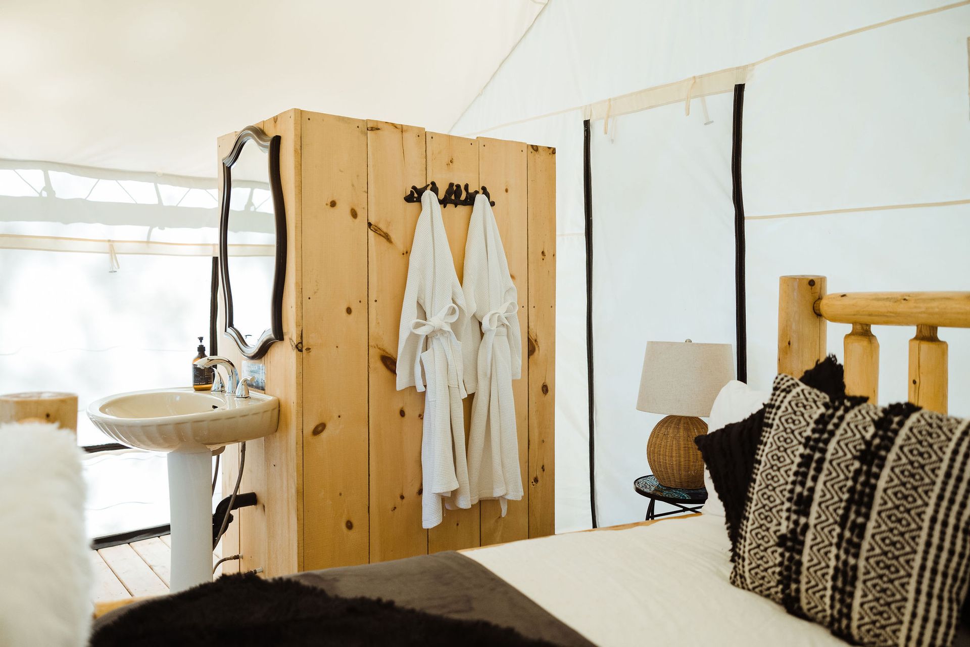 Bedroom interior: Rustic wood decor, robes hanging, bed with pillows, sink, white tent walls.