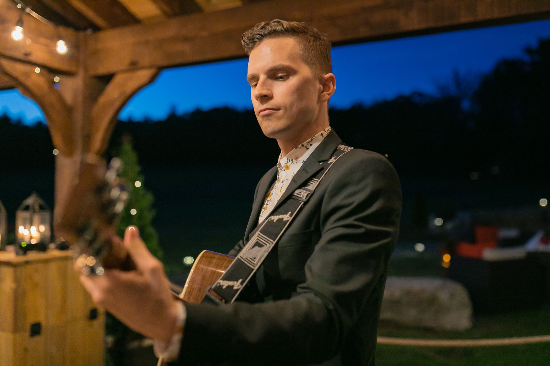 Man plays acoustic guitar outdoors at dusk.
