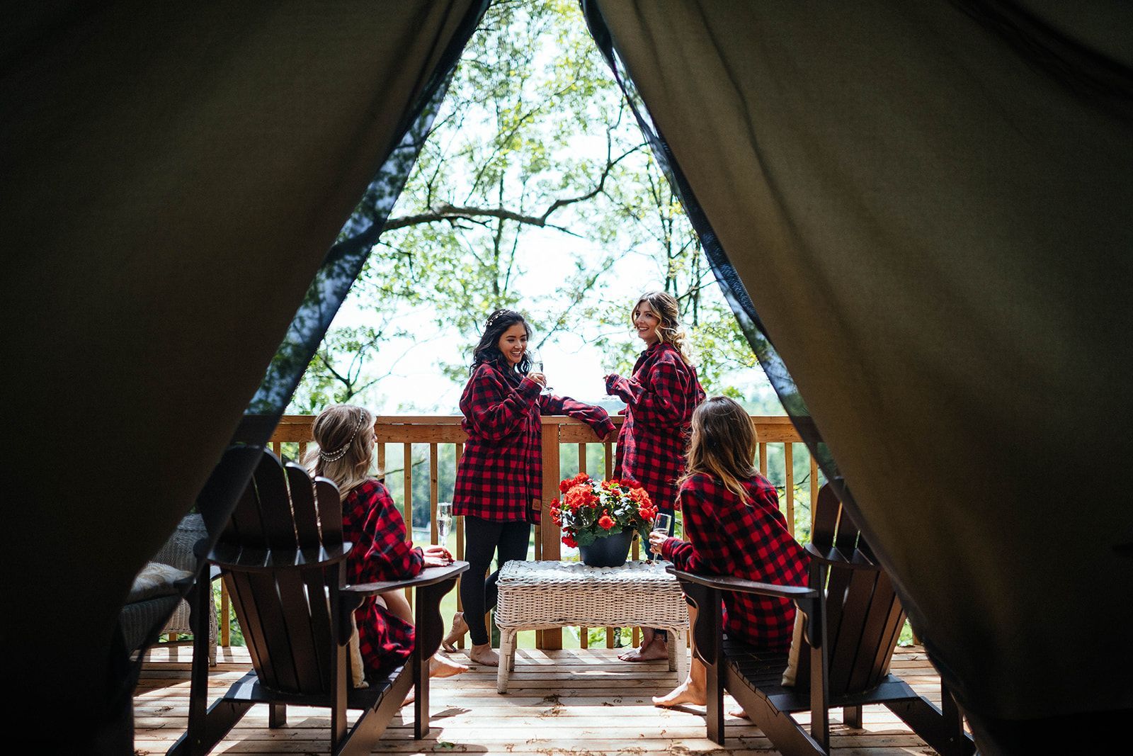 Four people in red plaid shirts on a wooden deck inside a tent. One at a small table, three in chairs.