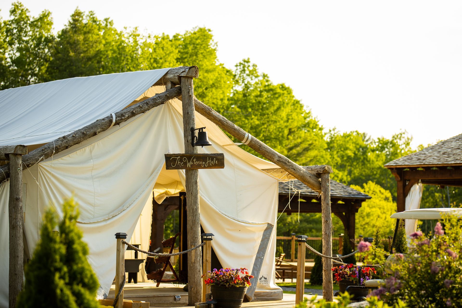 Canvas tent with wooden frame, set amongst trees and flowers.