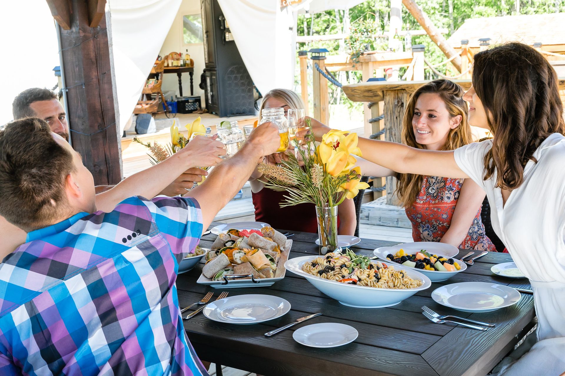 People toasting drinks at an outdoor table with food and flowers.