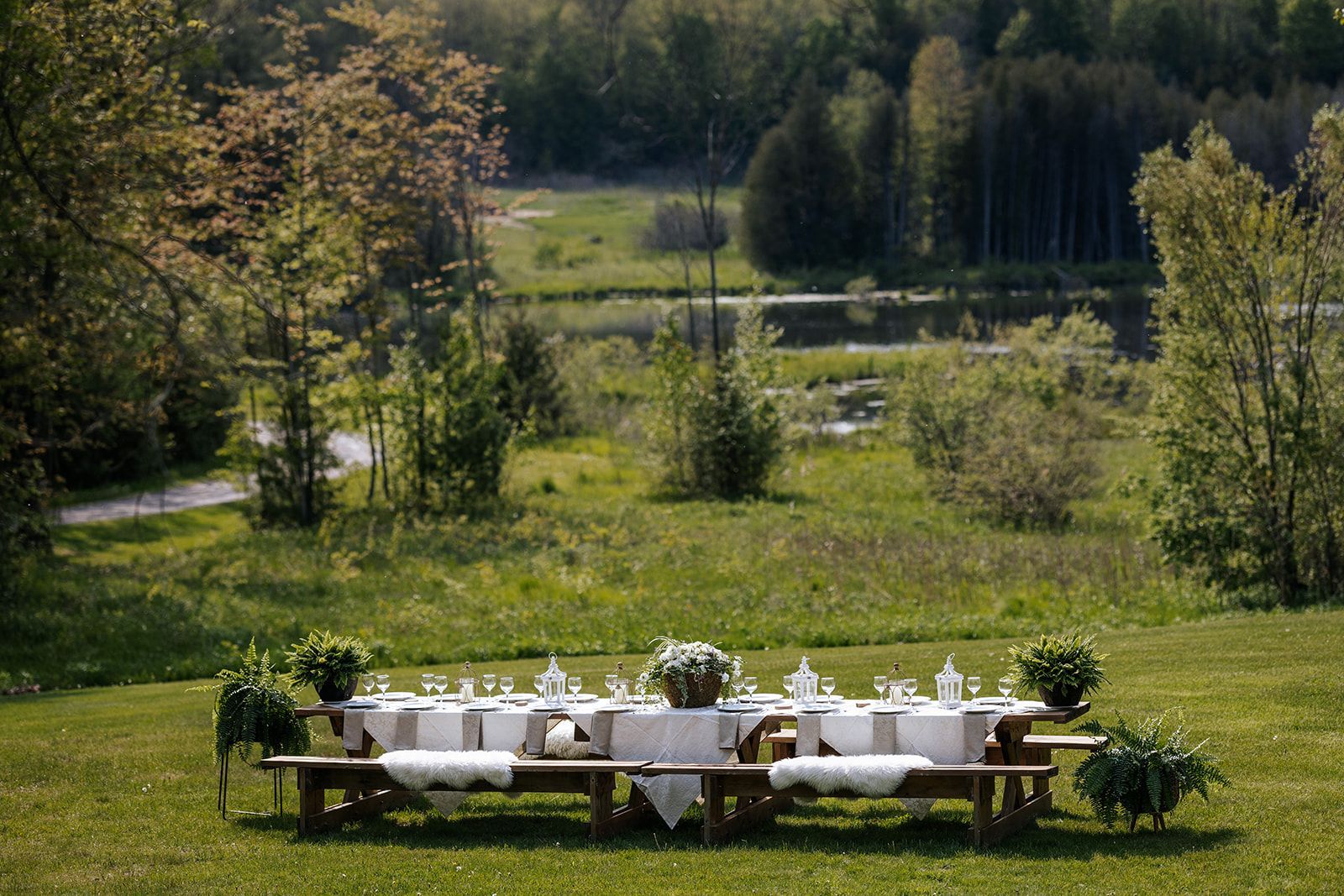 Picnic tables set with white tablecloths, overlooking a lake and forest.