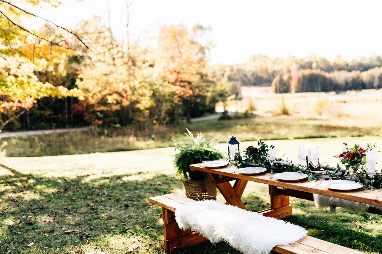 Picnic table set for dining outdoors, with floral arrangements and countryside view.