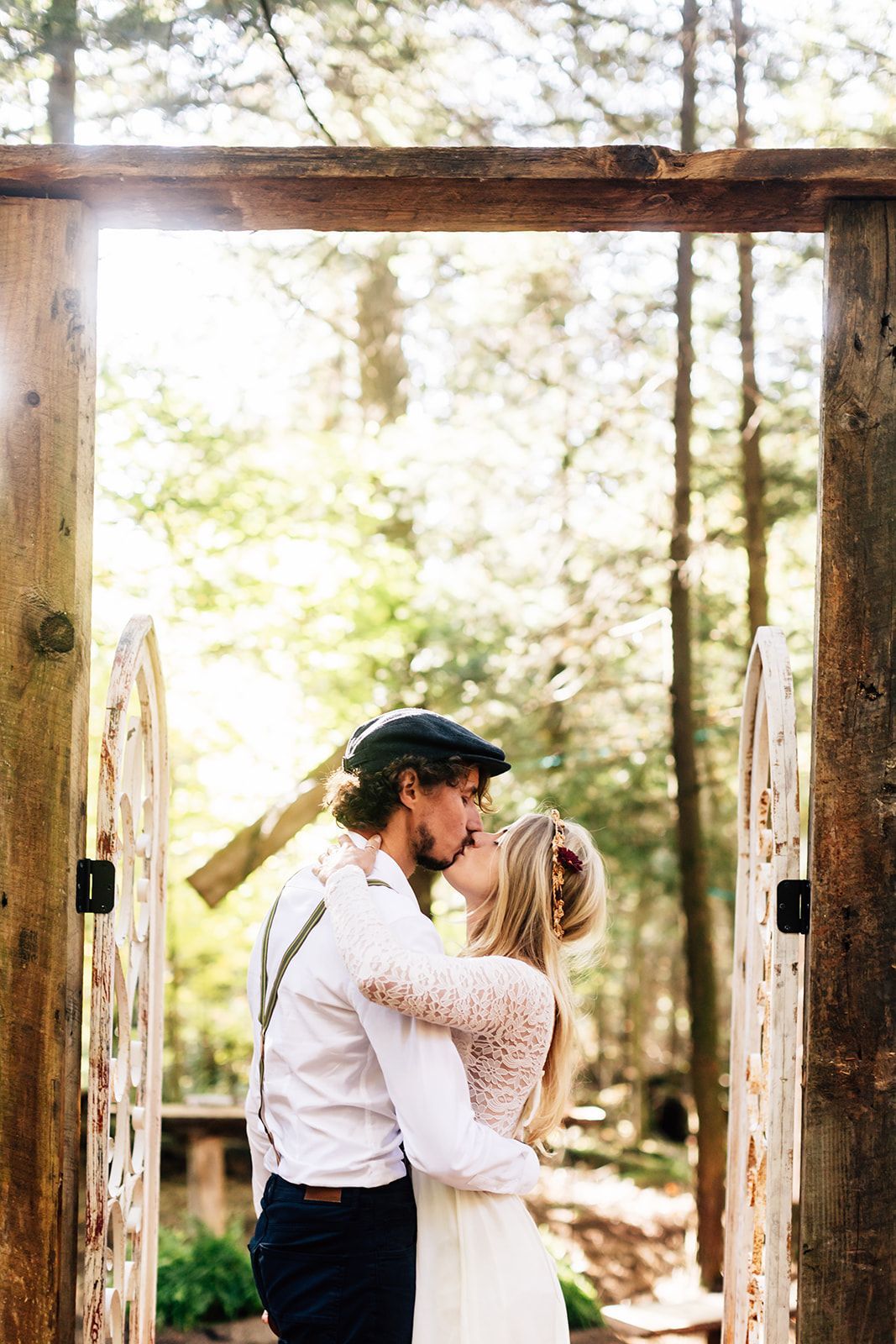 Couple kissing in front of a wooden archway in a forest.