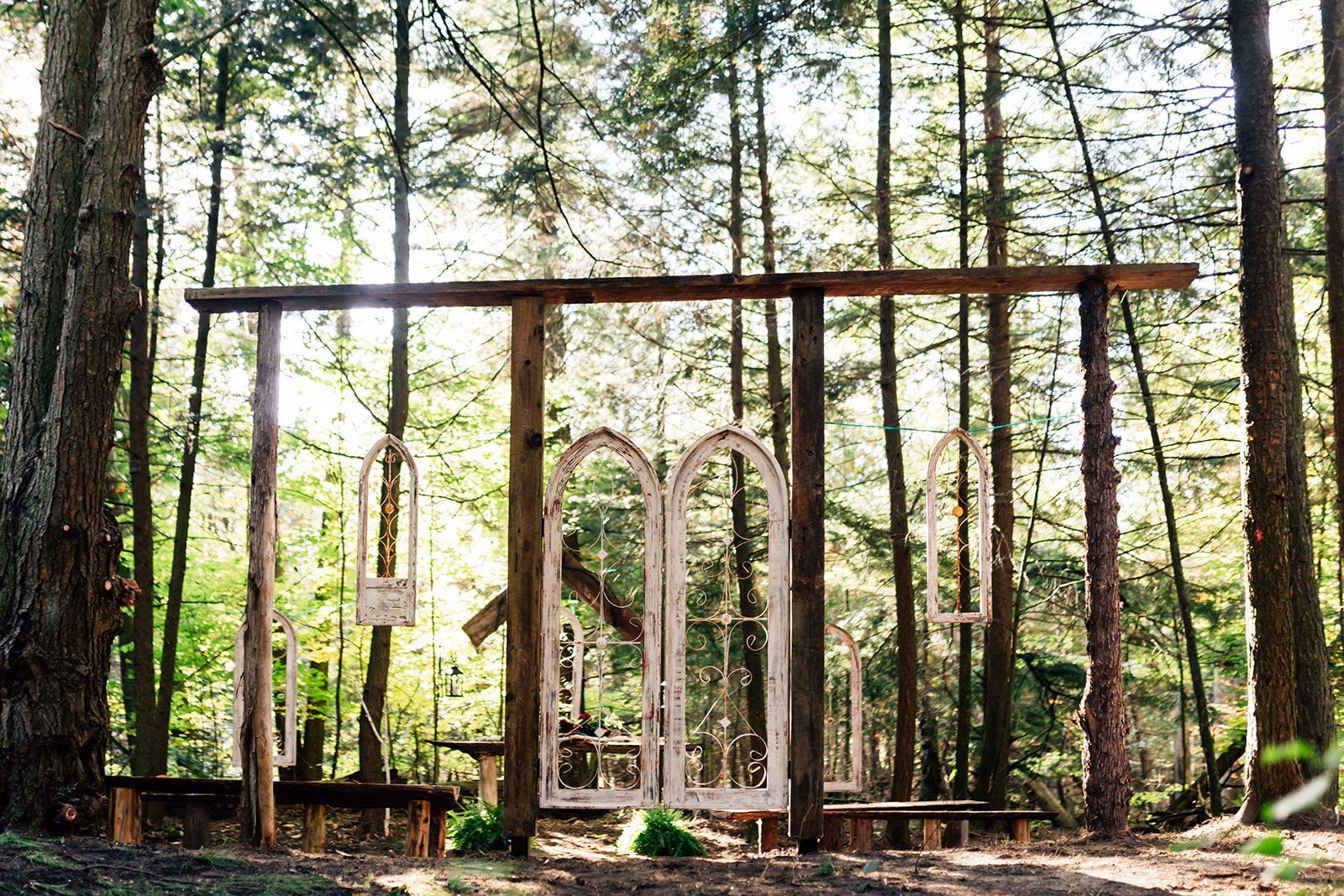 Wooden frame with repurposed windows in a forest setting, used for a ceremony backdrop.