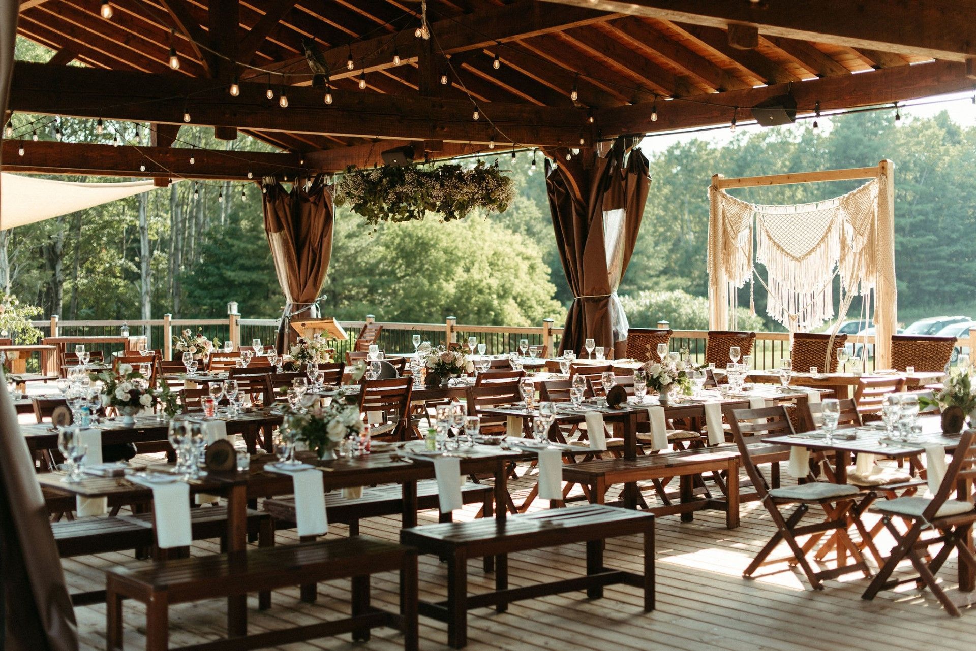 Outdoor wedding reception with long tables, string lights, and macrame backdrop.