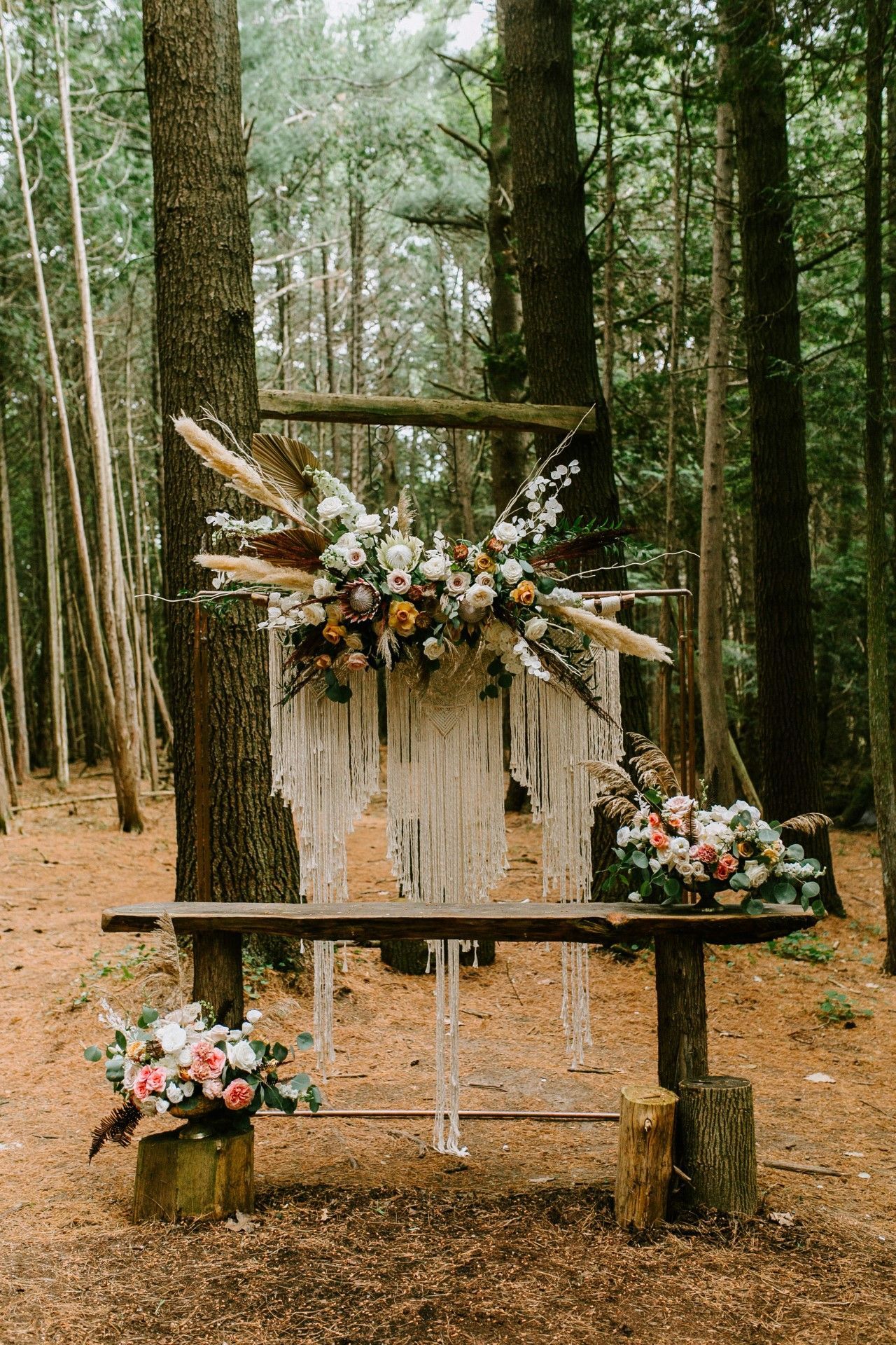 Wooden wedding altar in a forest, decorated with flowers and macrame.
