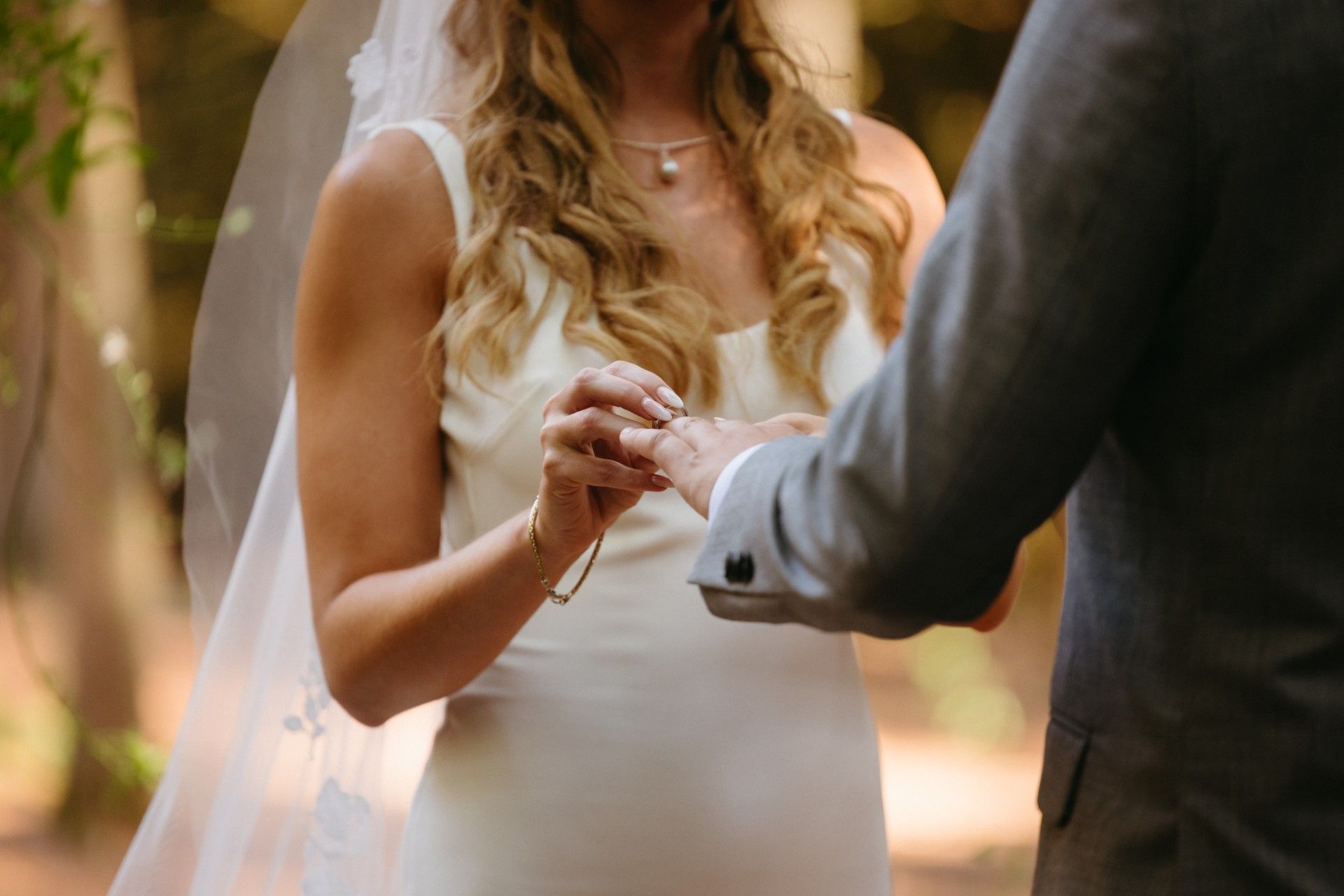 Bride putting ring on groom's finger during outdoor wedding ceremony.