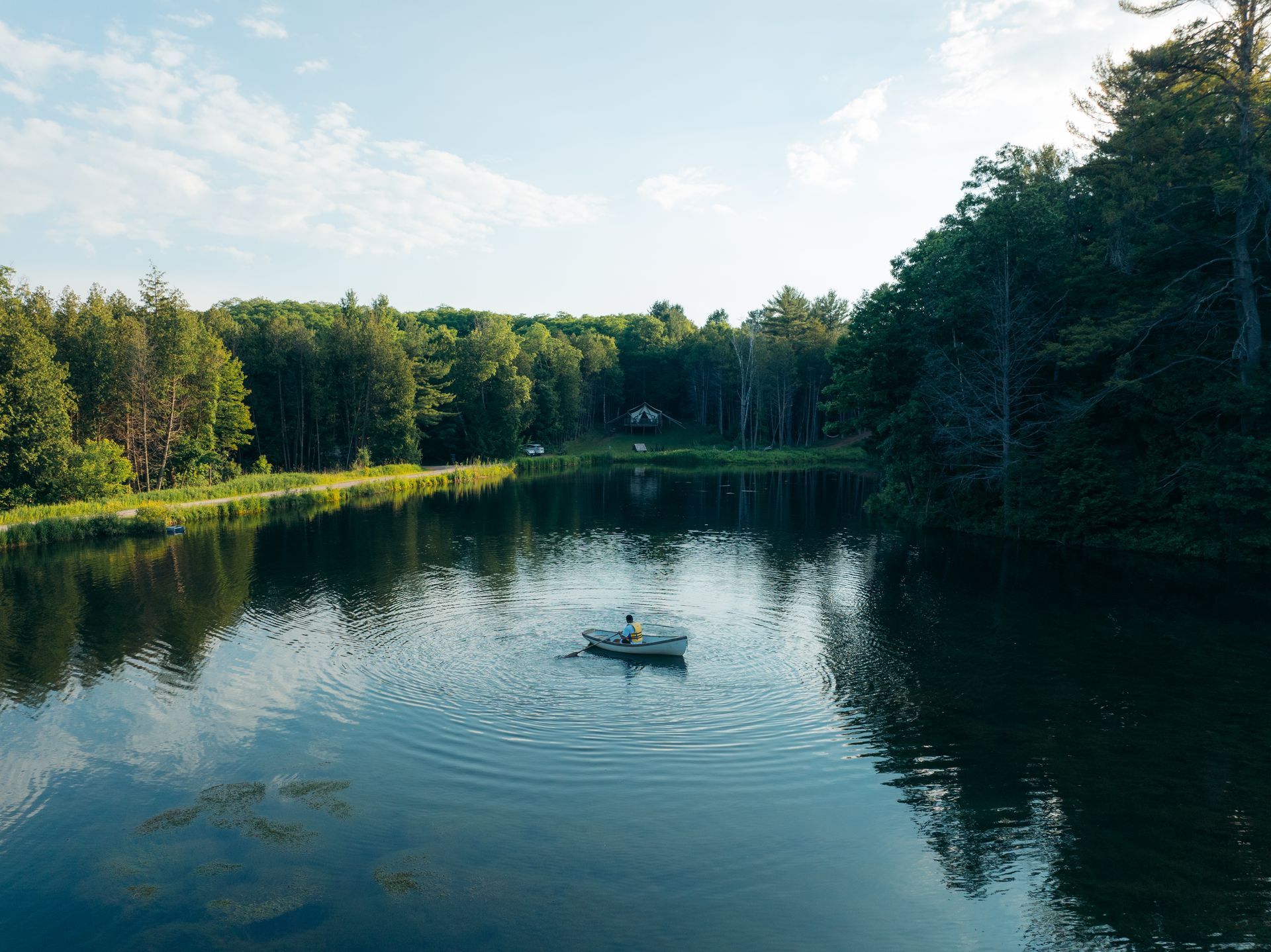 Small boat on calm lake, surrounded by trees under a blue sky.