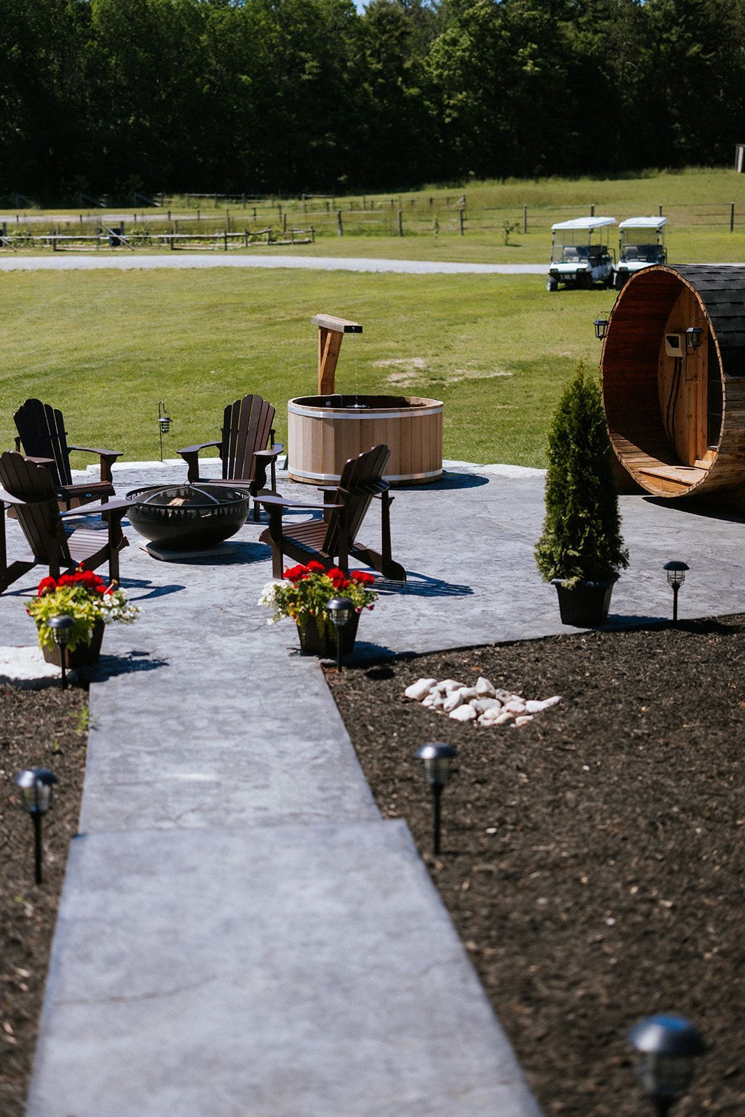 Outdoor patio with Adirondack chairs, fire pit, hot tub, and barrel sauna; golf carts in background.