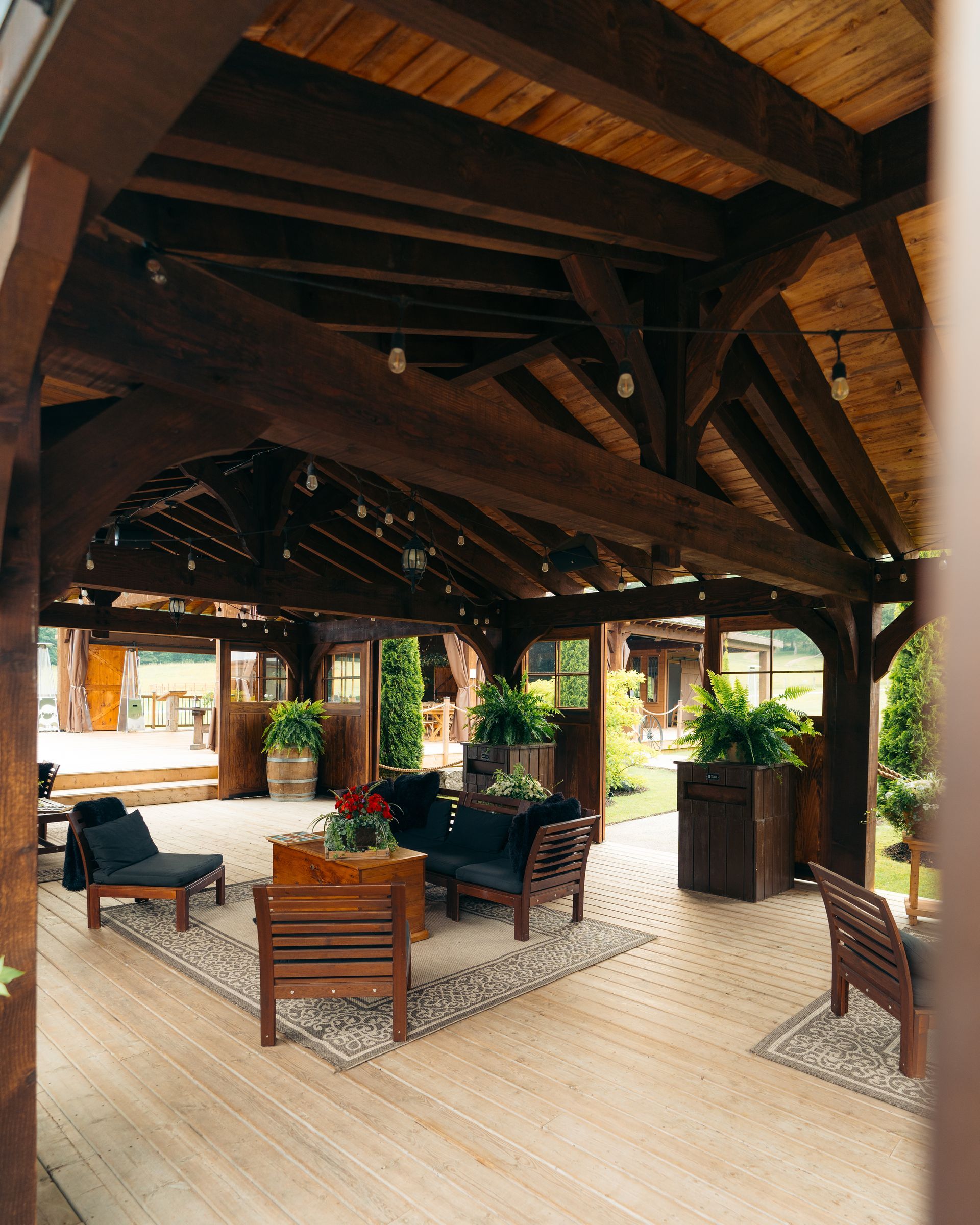 Wooden-beamed outdoor patio with seating, plants, and string lights; a cozy, inviting space.