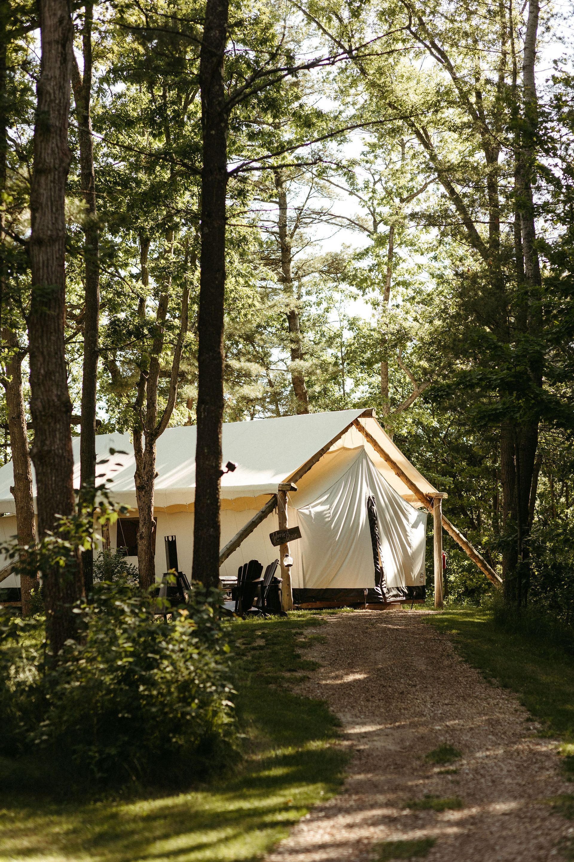 Canvas tent in a wooded area; gravel path leads to the entrance.