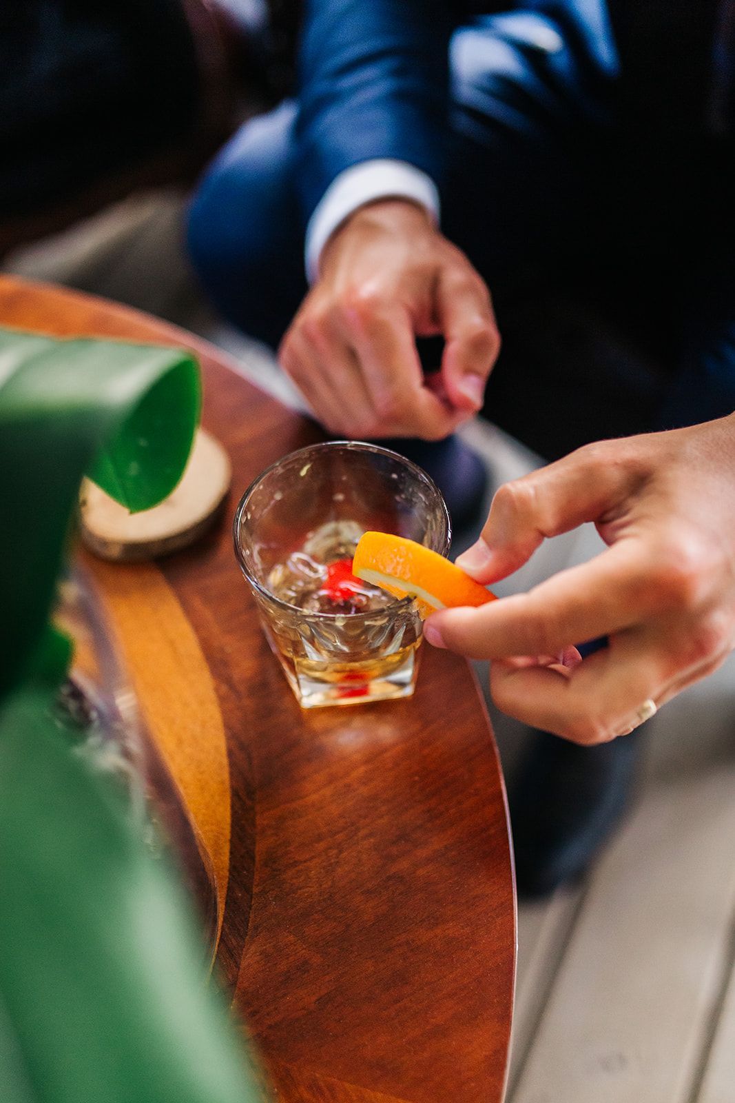 Man garnishing a cocktail with an orange slice on a wooden surface.