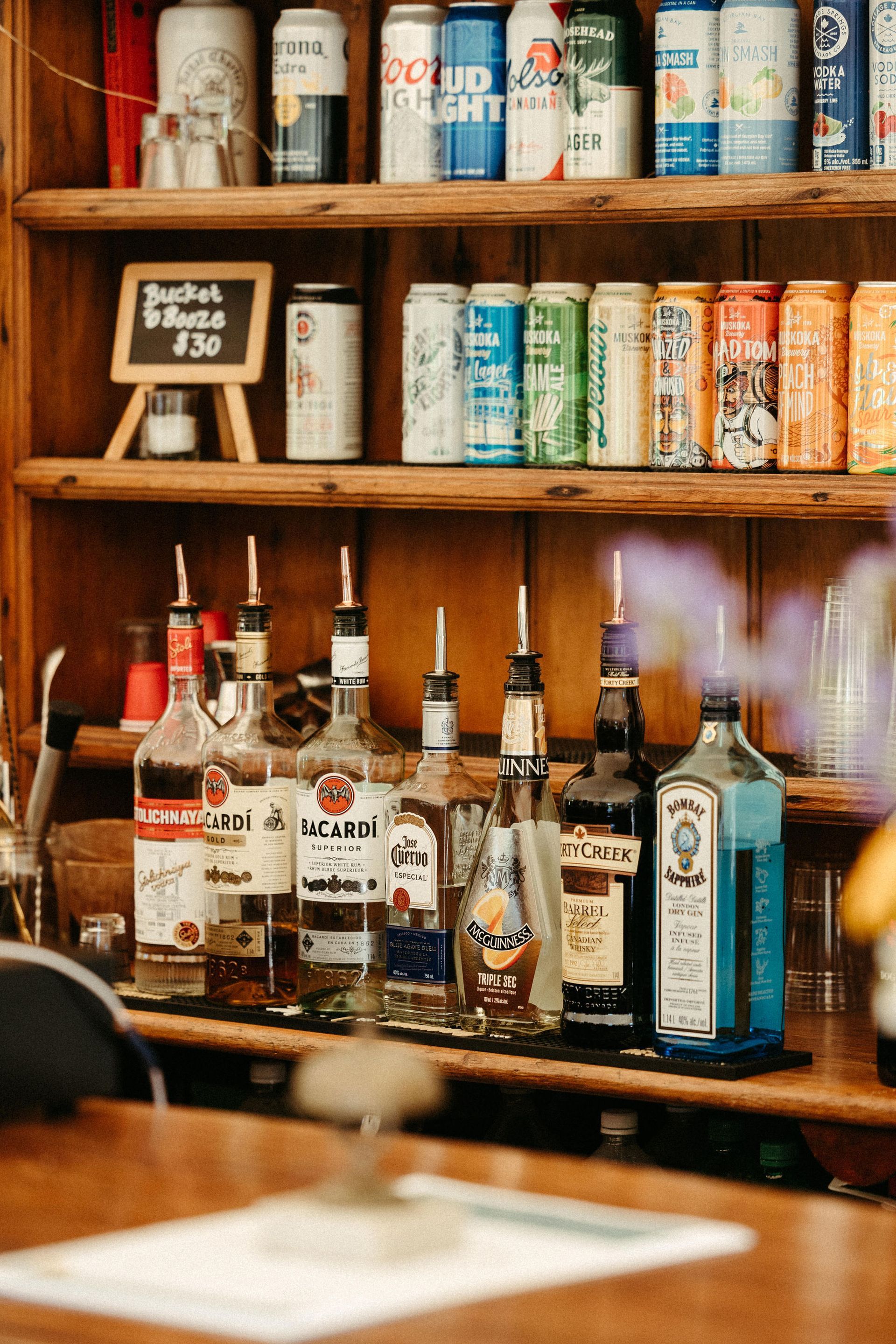 Bar with liquor bottles and beer cans on shelves; wooden interior.