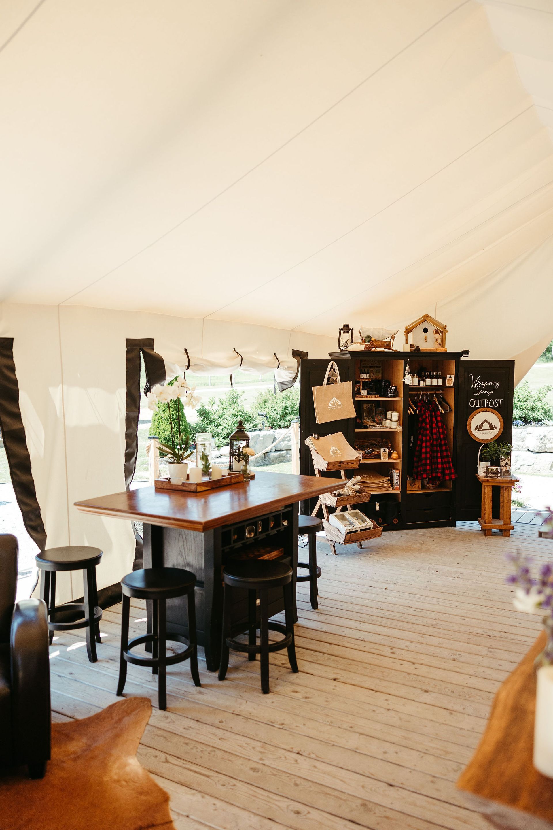 Interior of a large tent with a kitchen island, bar stools, and a wooden display cabinet.