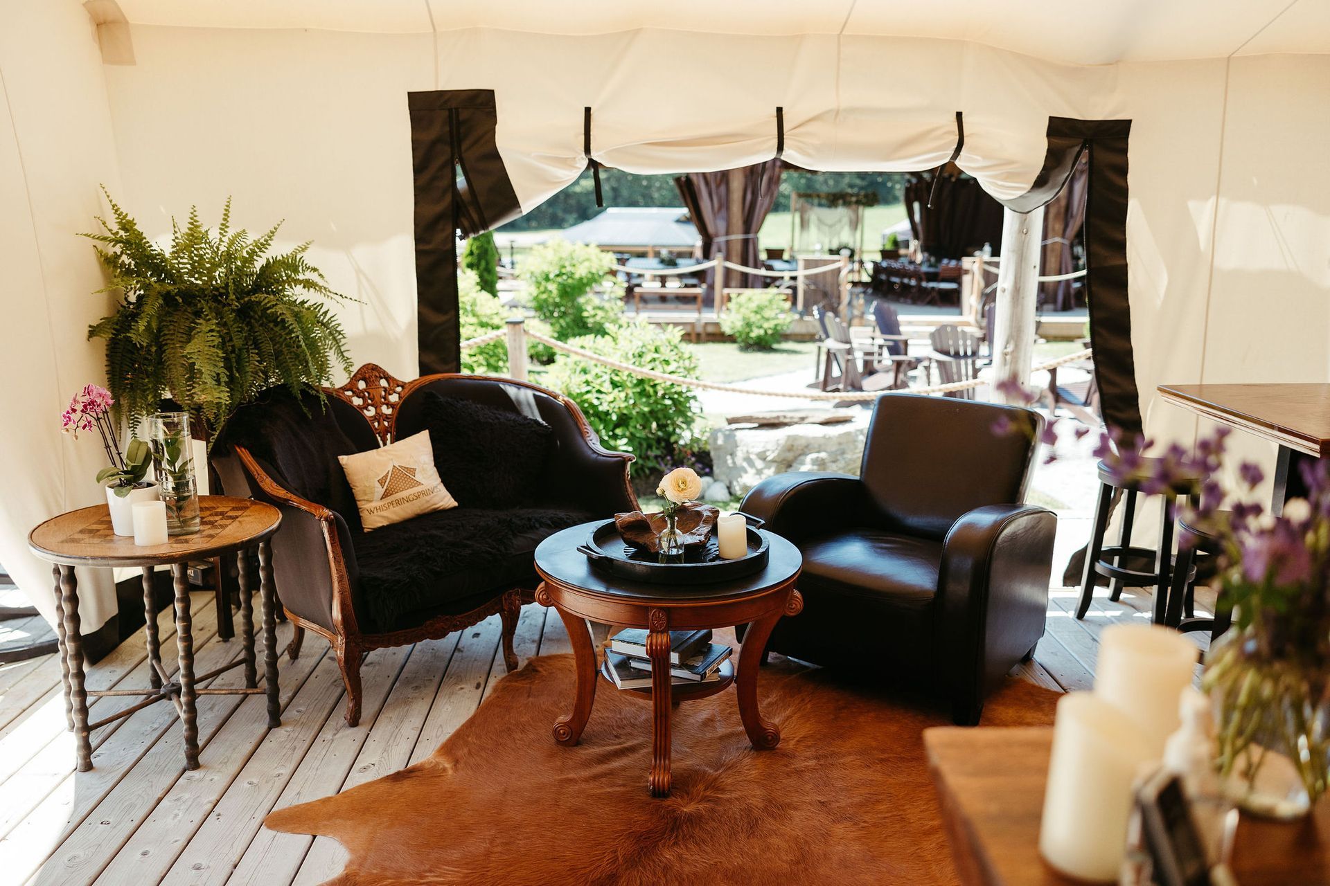 Interior of a tent with vintage furniture, animal-hide rug, and an open view of a patio and greenery.